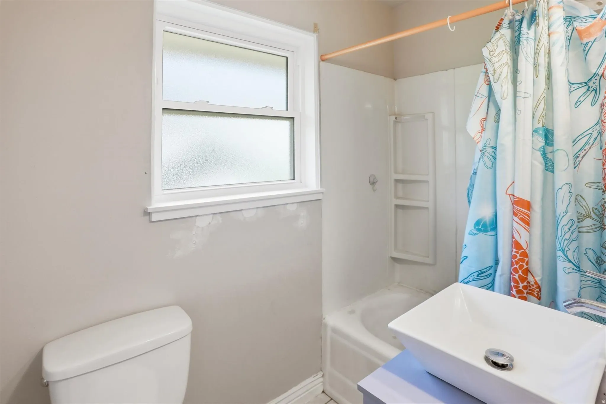 White bathtub with integrated shelving, a white rectangular vessel sink, and a white-framed window with privacy glass