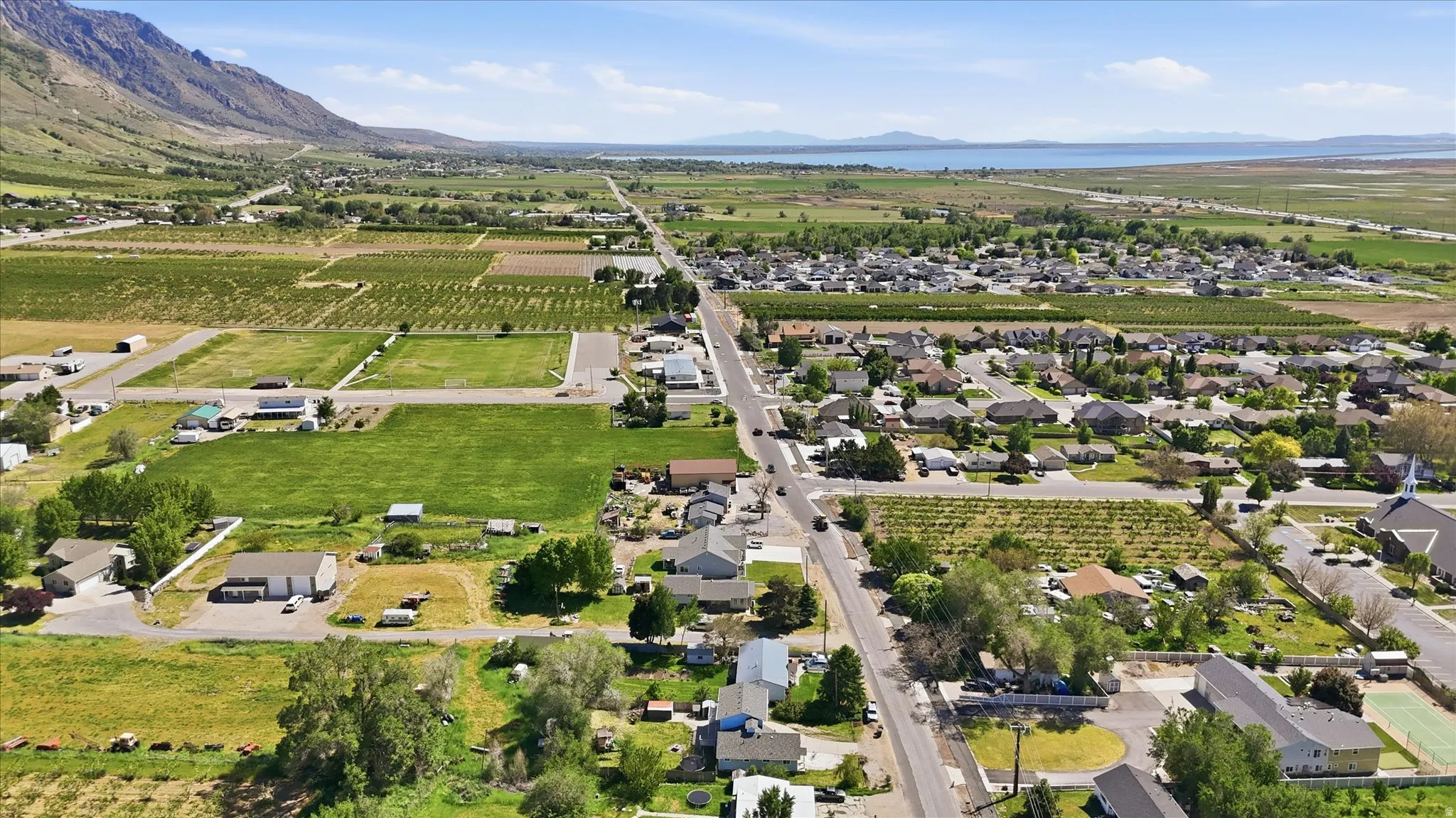 Expansive aerial landscape highlighting a developed residential area with a prominent mountain range backdrop and a large body of water in the distance