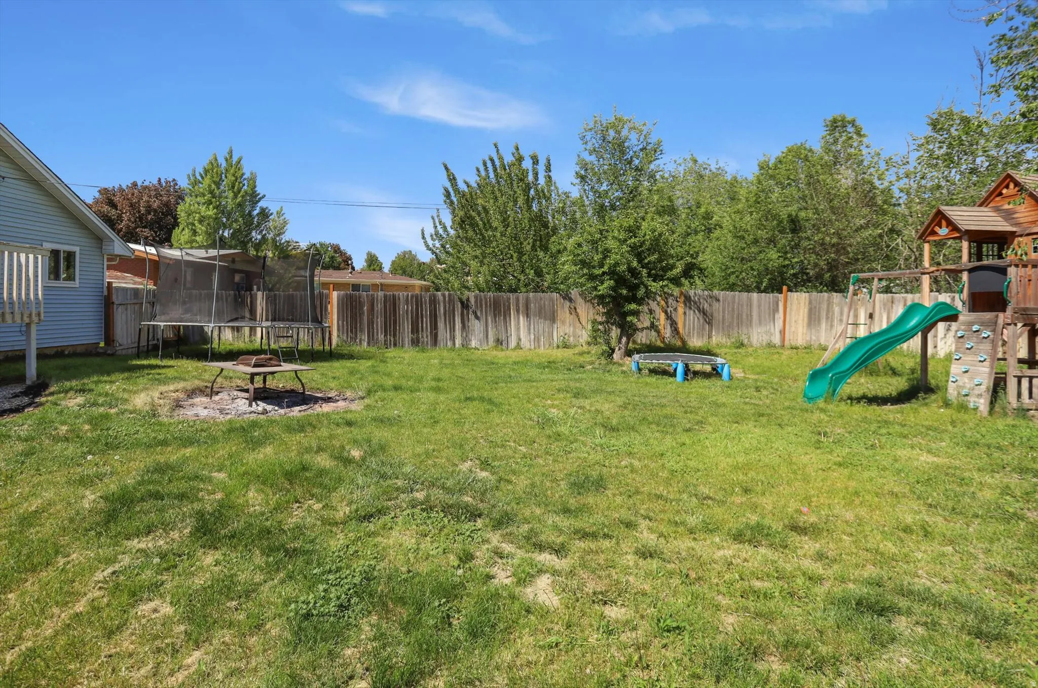 Expansive grassy backyard featuring a wooden privacy fence, mature trees, and a visible side of the property with light blue siding