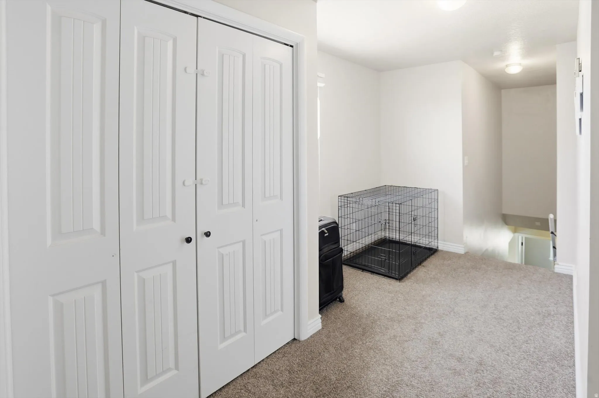 Recessed lighting illuminates this landing featuring white walls, textured carpeting, and a built-in closet with paneled bifold doors