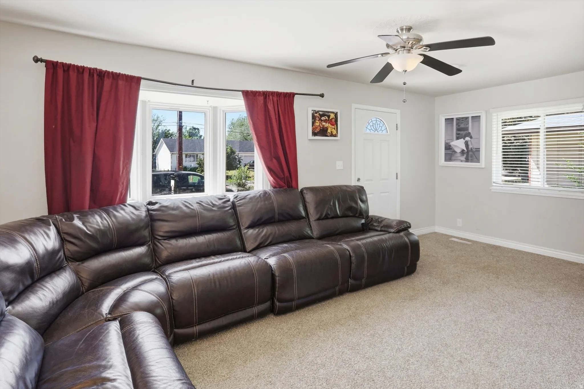 Living area featuring a textured carpet, a ceiling fan with integrated lighting, and a white entry door with an arched window insert