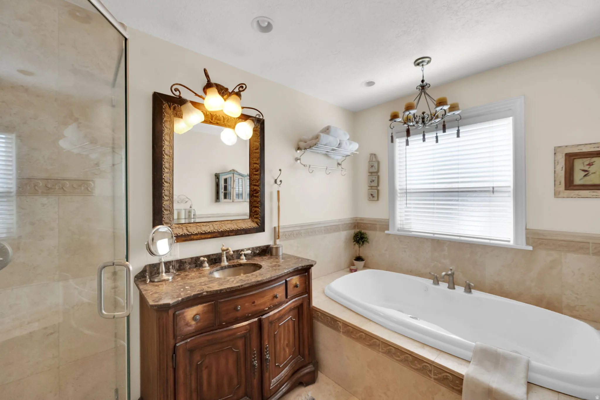 Bathroom featuring a freestanding tub, glass-enclosed shower, a vanity with a stone countertop, and a decorative chandelier