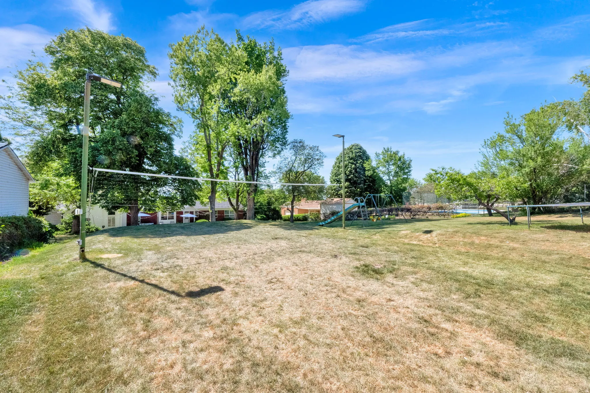 Backyard featuring a volleyball net, mature trees, and open lawn space