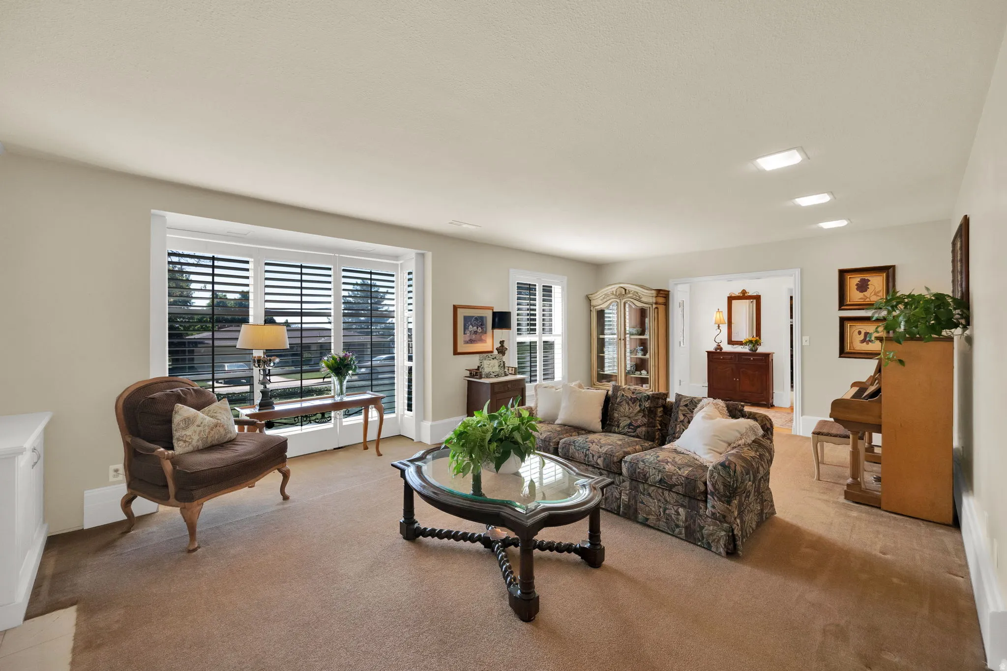 Spacious living area featuring carpet flooring, recessed ceiling lighting, and large windows with integrated plantation shutters