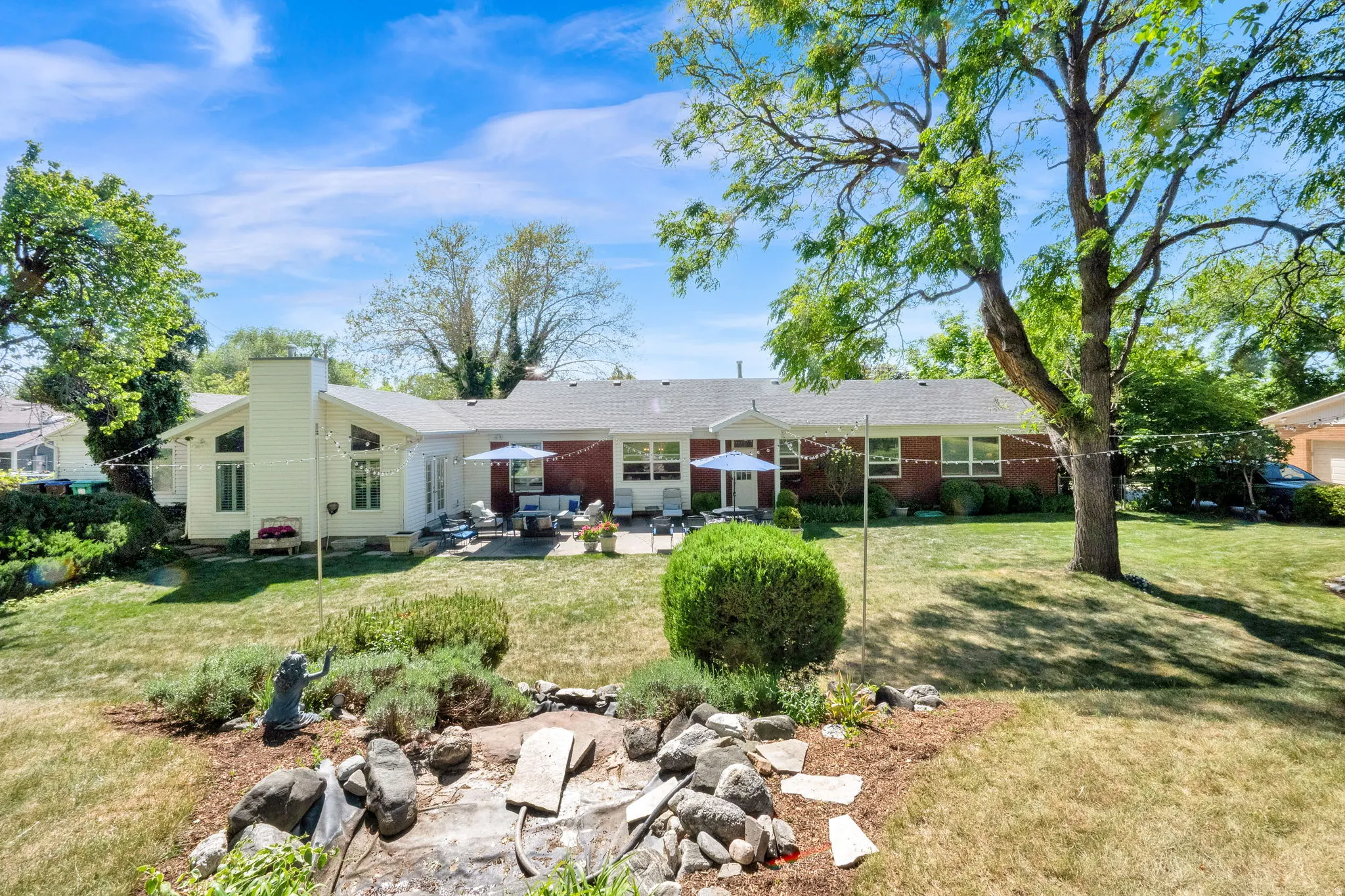 Expansive backyard featuring a large patio, mature trees, and a rock water feature