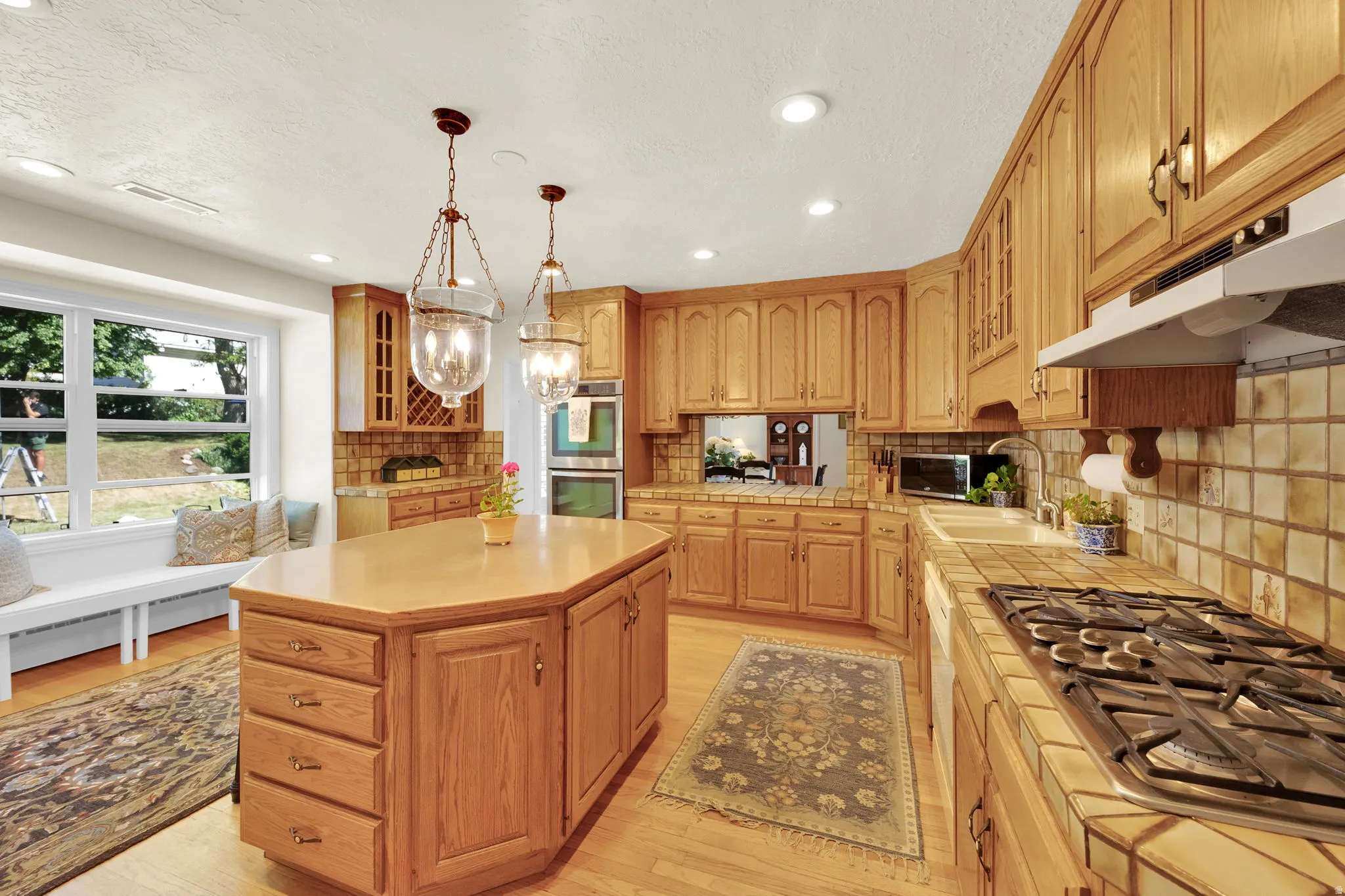Kitchen featuring wood-finish cabinetry, an octagonal island with storage, tile countertops, and a gas range