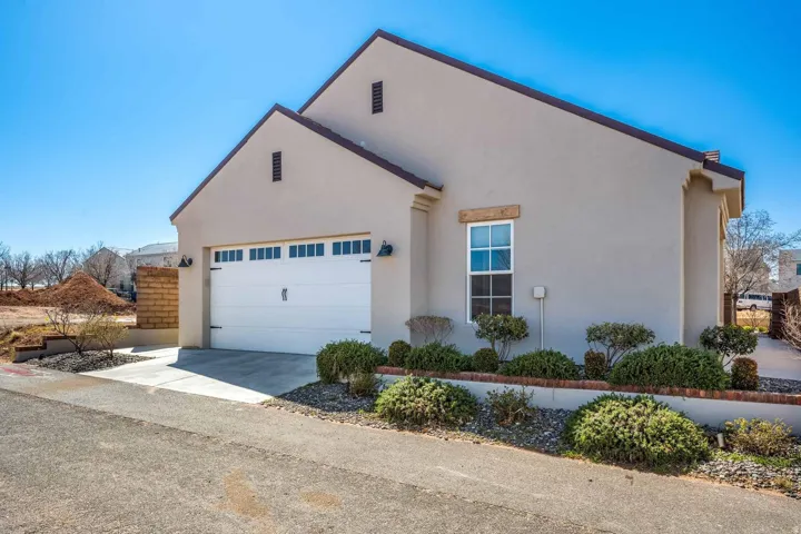 Stucco exterior featuring a pitched roofline, an attached garage with a panel door and window inserts, and sconce lighting