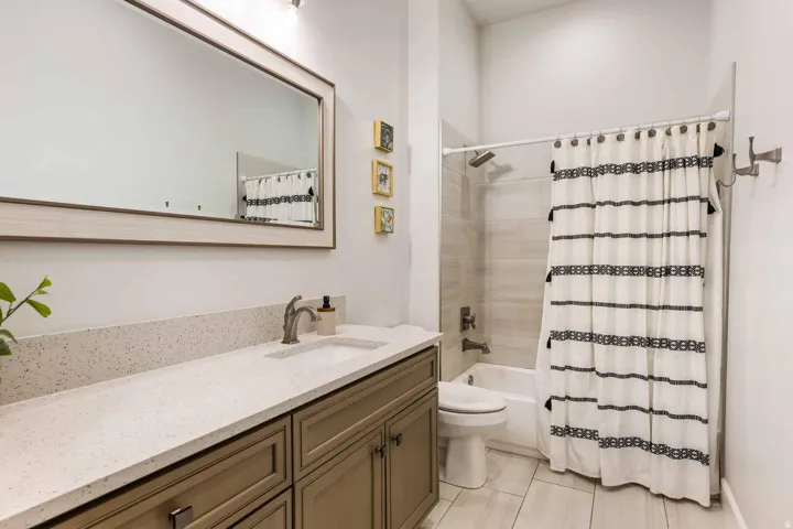 Bathroom featuring a neutral color palette, a rectangular framed mirror, a vanity with a light-colored countertop, and a shower-over-tub combination with a tiled surround
