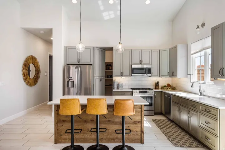 Modern kitchen featuring a wood-finish island with a white countertop, stainless steel appliances, light gray cabinetry, subway tile backsplash, and recessed lighting