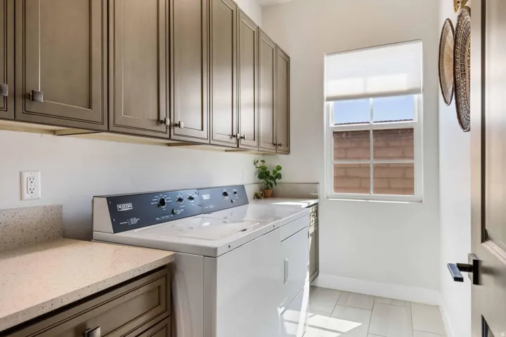Dedicated laundry space featuring extensive upper cabinetry, light-toned countertops, and a window with a roller shade