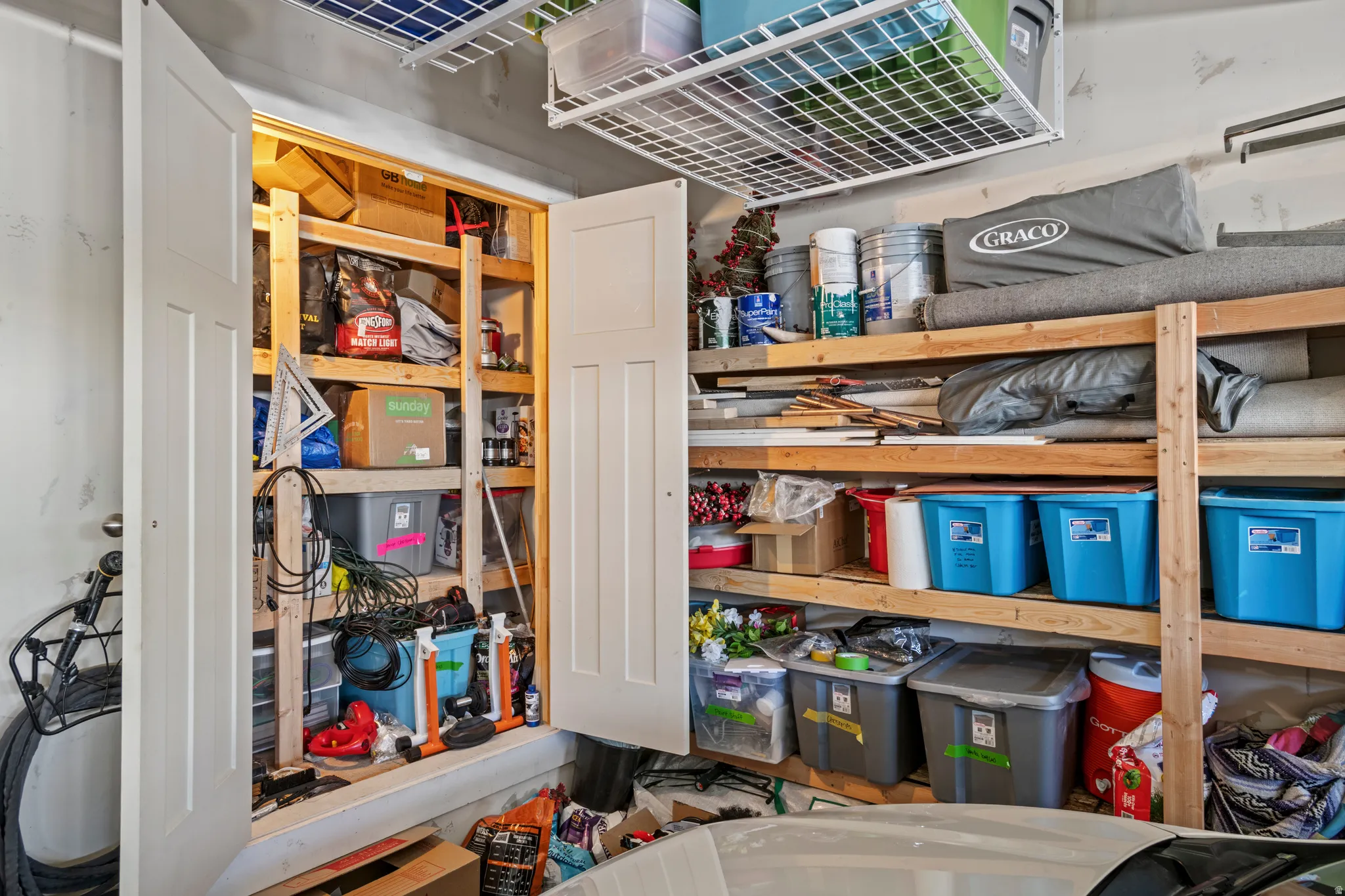 Garage storage solutions featuring built-in wooden shelving, an overhead metal storage rack, and a dedicated storage closet with bi-fold doors