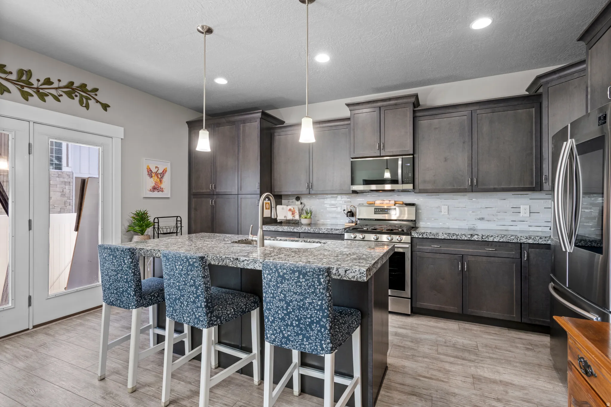 Upgraded kitchen featuring shaker-style cabinetry, stainless steel appliances, gas stove, and granite countertops. Note French doors to covered patio.