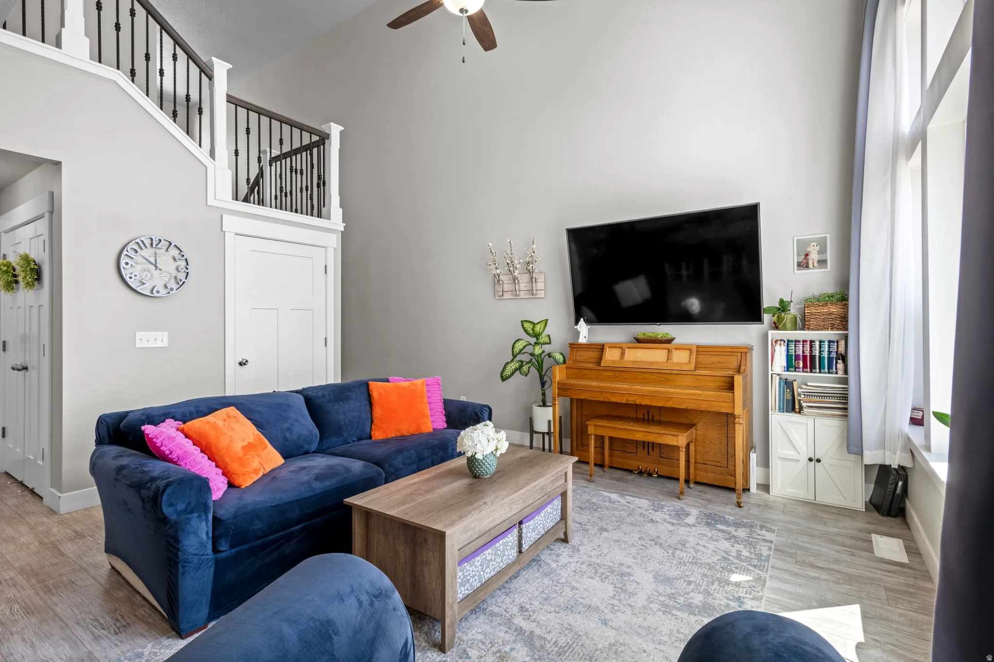 Two-story living area featuring vaulted ceilings, upgraded laminate flooring, ceiling fan, and white trim. Note door to basement behind sofa.