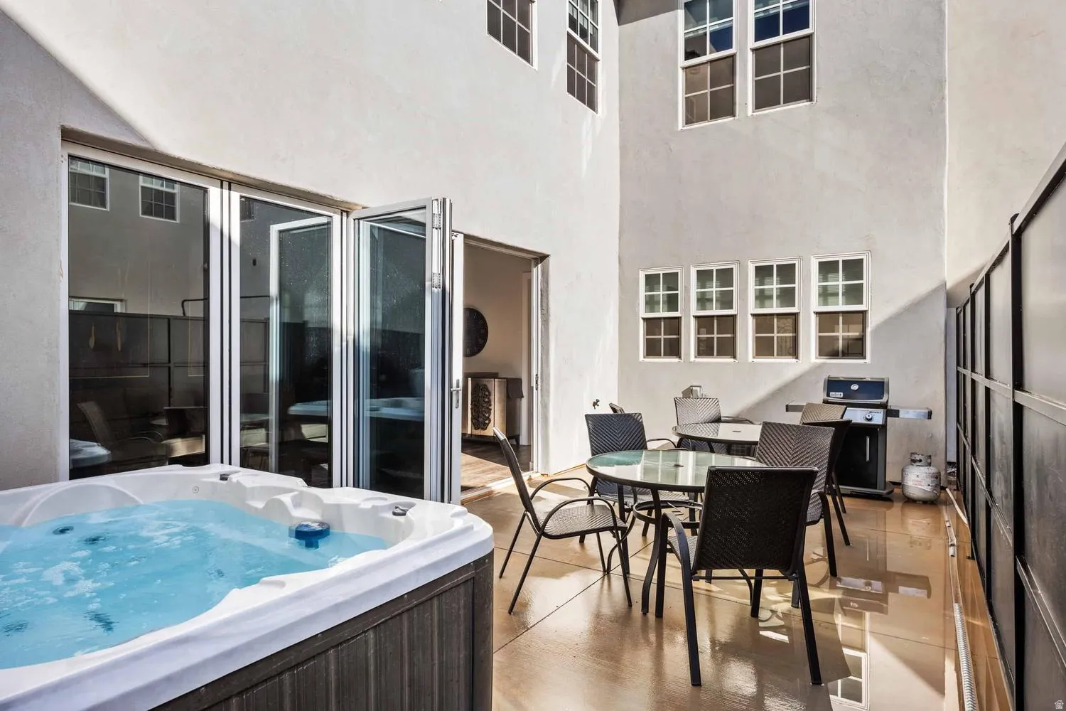 Outdoor patio featuring a built-in spa with wood-finish siding, bi-fold glass doors, and a concrete patio surface