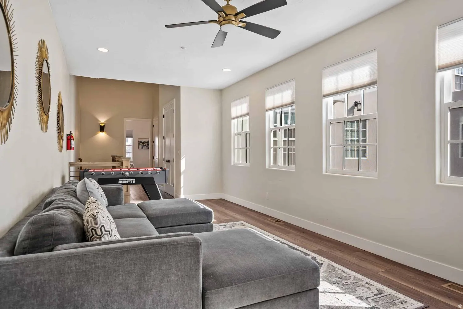 Spacious room featuring multiple windows with blinds, recessed lighting, wood-finish flooring, and a ceiling fan with brass accents