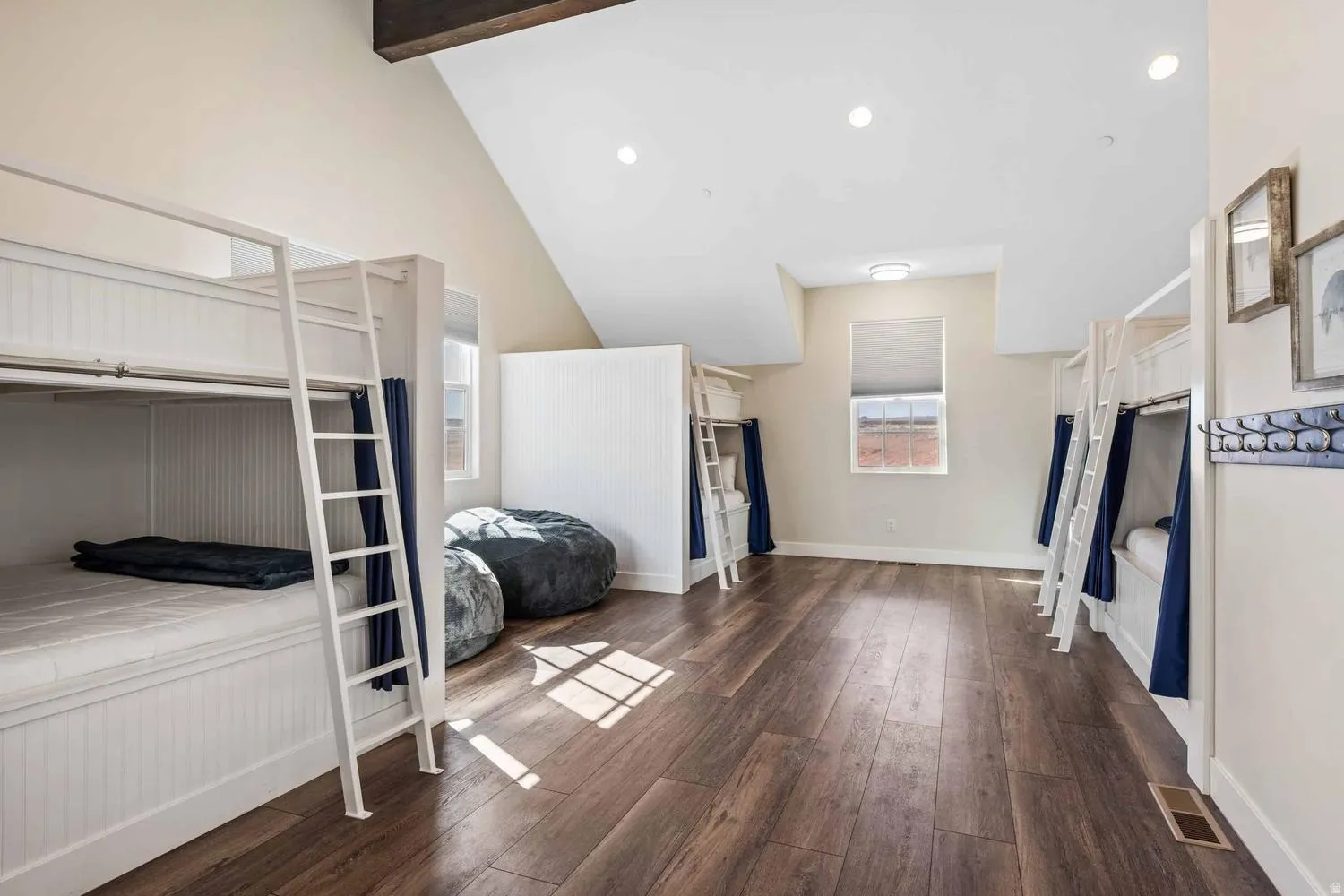 Spacious room featuring multiple built-in bunk beds with individual privacy curtains, wood-finish flooring, recessed lighting, and an exposed ceiling beam