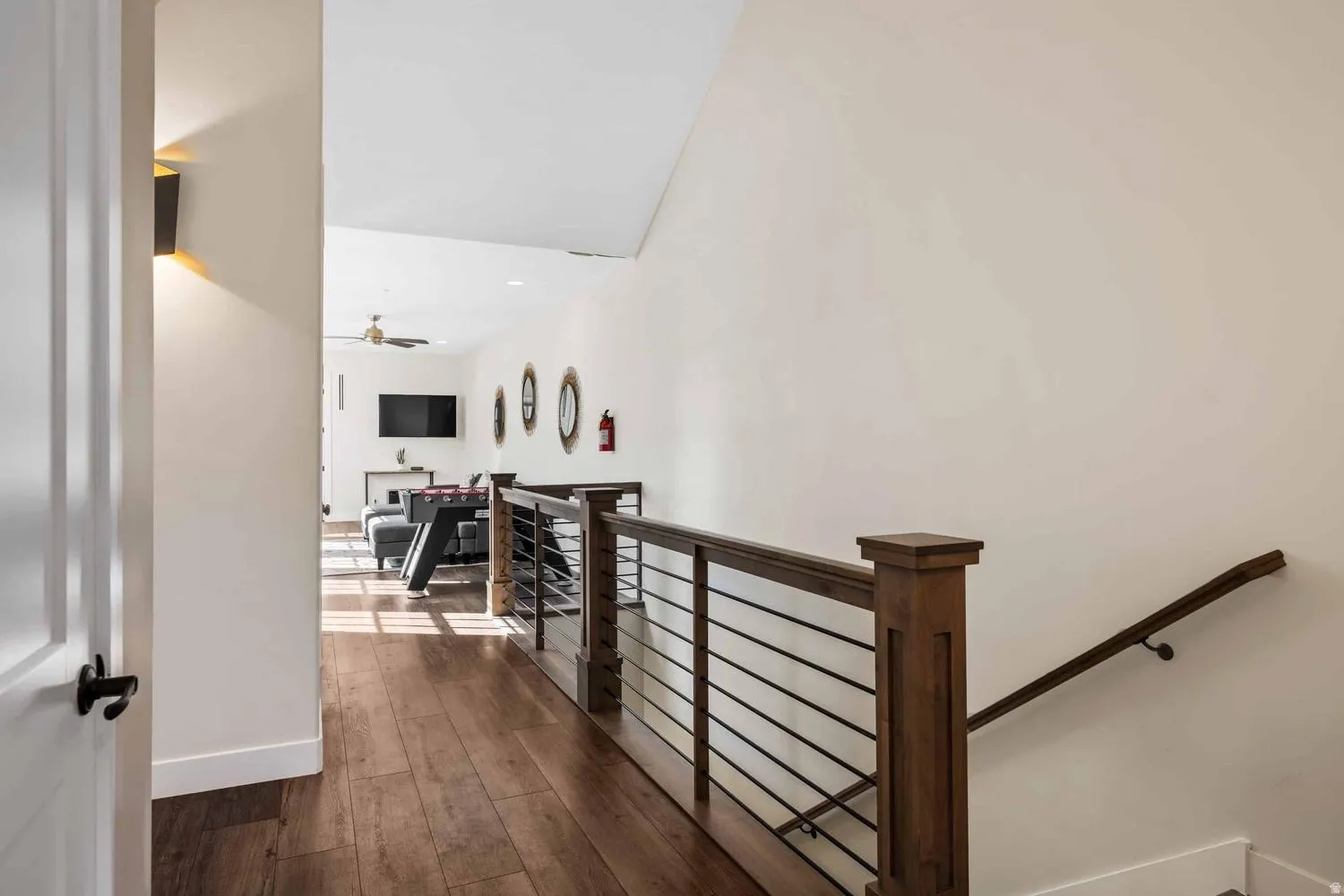 Upper-level landing featuring wood-finish flooring, a contemporary wood and metal railing, and a wall-mounted sconce