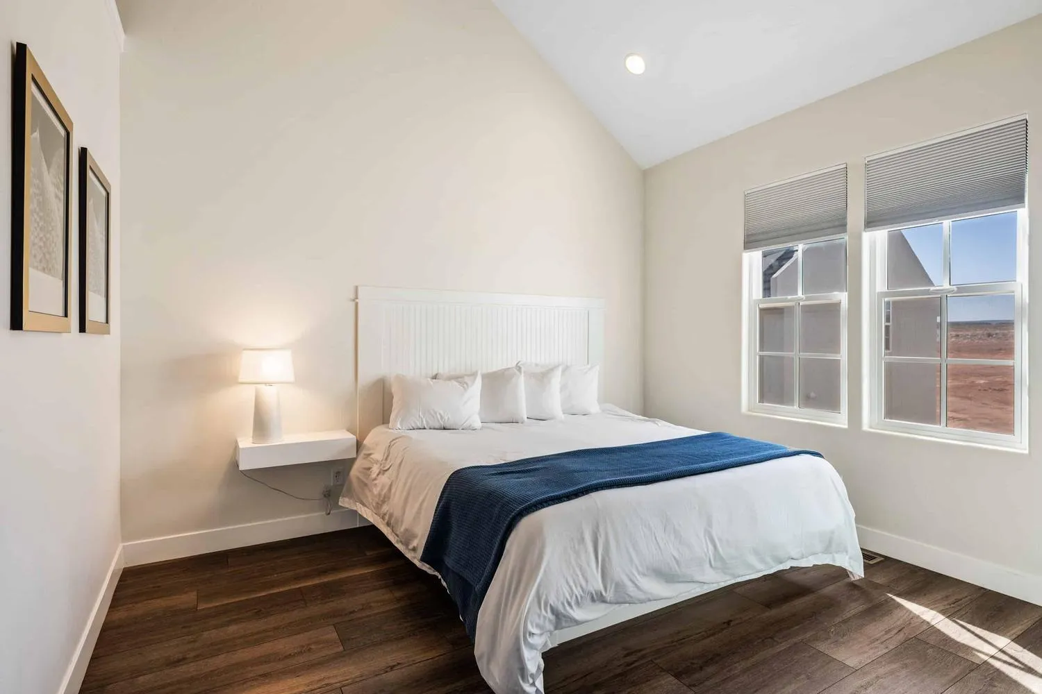 Vaulted ceiling room featuring wood-finish flooring, two large windows with cellular shades, and a built-in floating nightstand