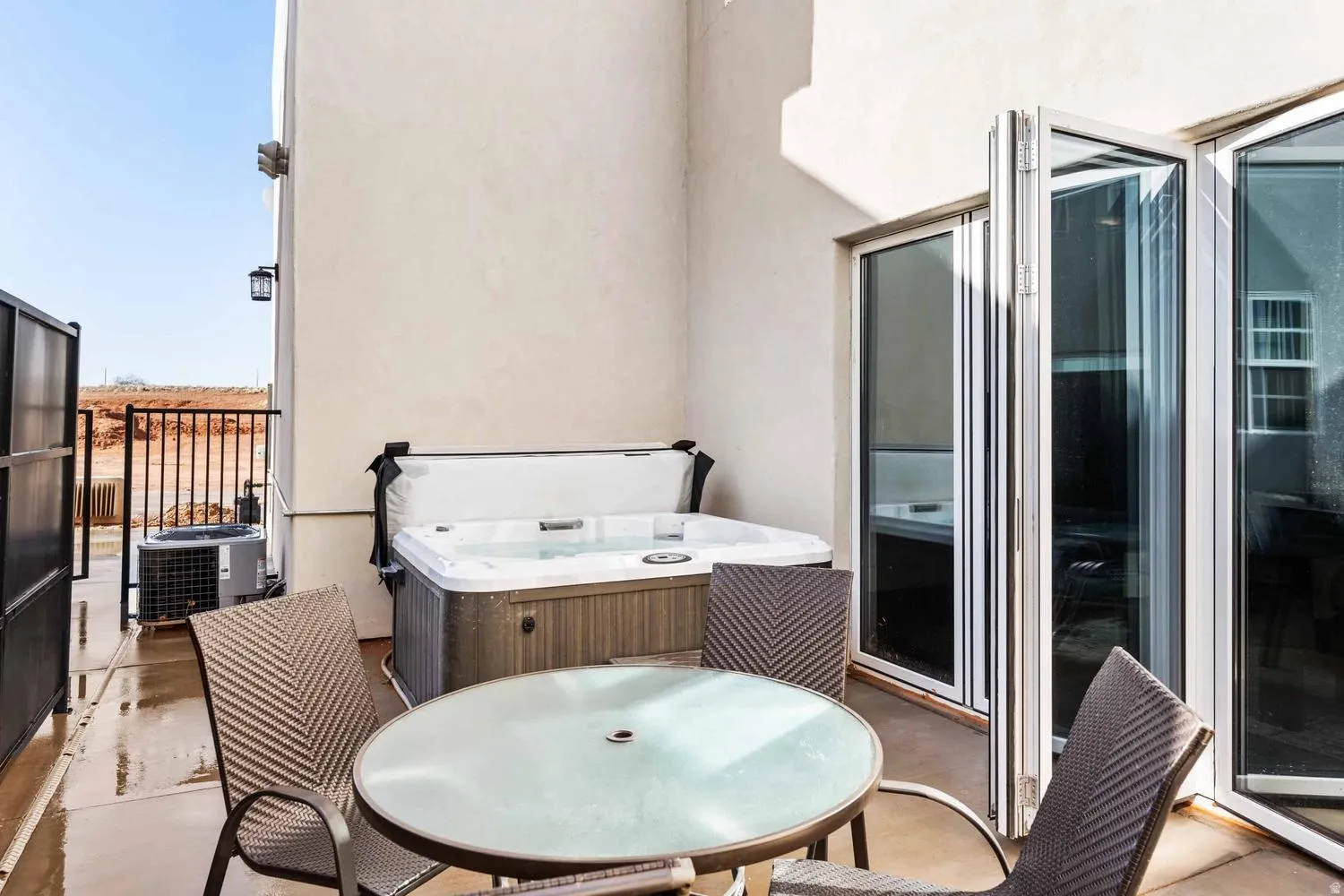 Private patio featuring a built-in hot tub, concrete flooring, and folding glass doors