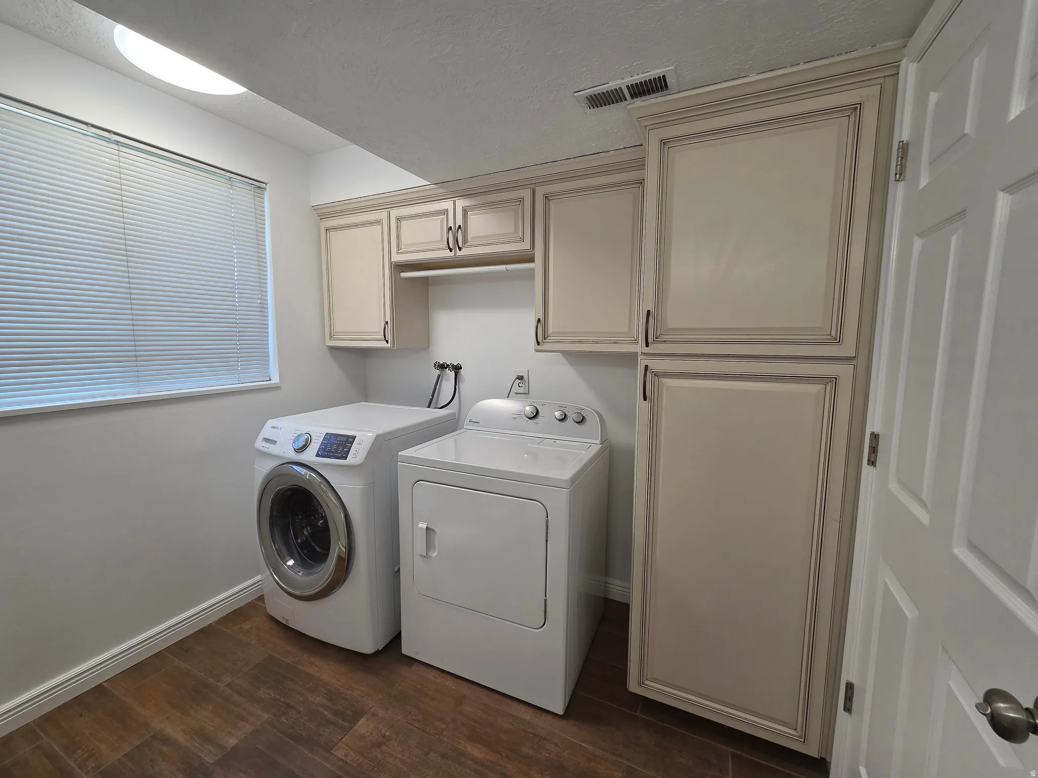 Dedicated utility space featuring extensive cabinetry, wood-finish flooring, a window with blinds, and ceiling illumination