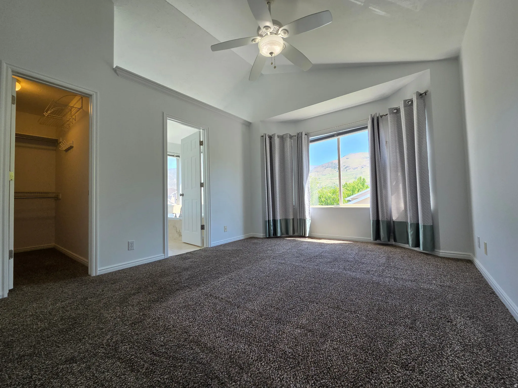 Spacious room featuring vaulted ceilings and a ceiling fan, bay windows, and neutral carpet flooring