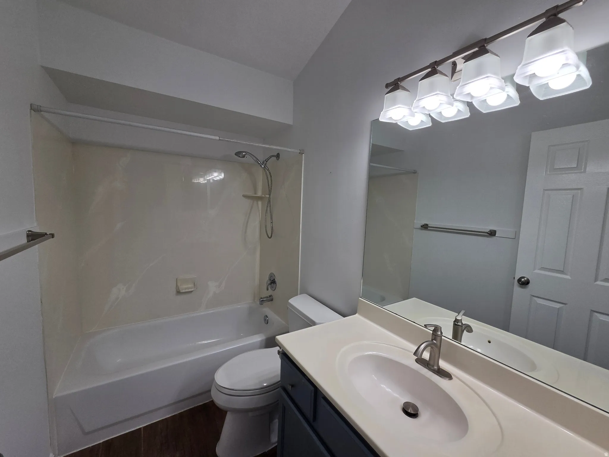 Bathroom featuring a combination shower and tub with a white surround, a single vanity with an integrated sink and light countertop, and wood-finish flooring