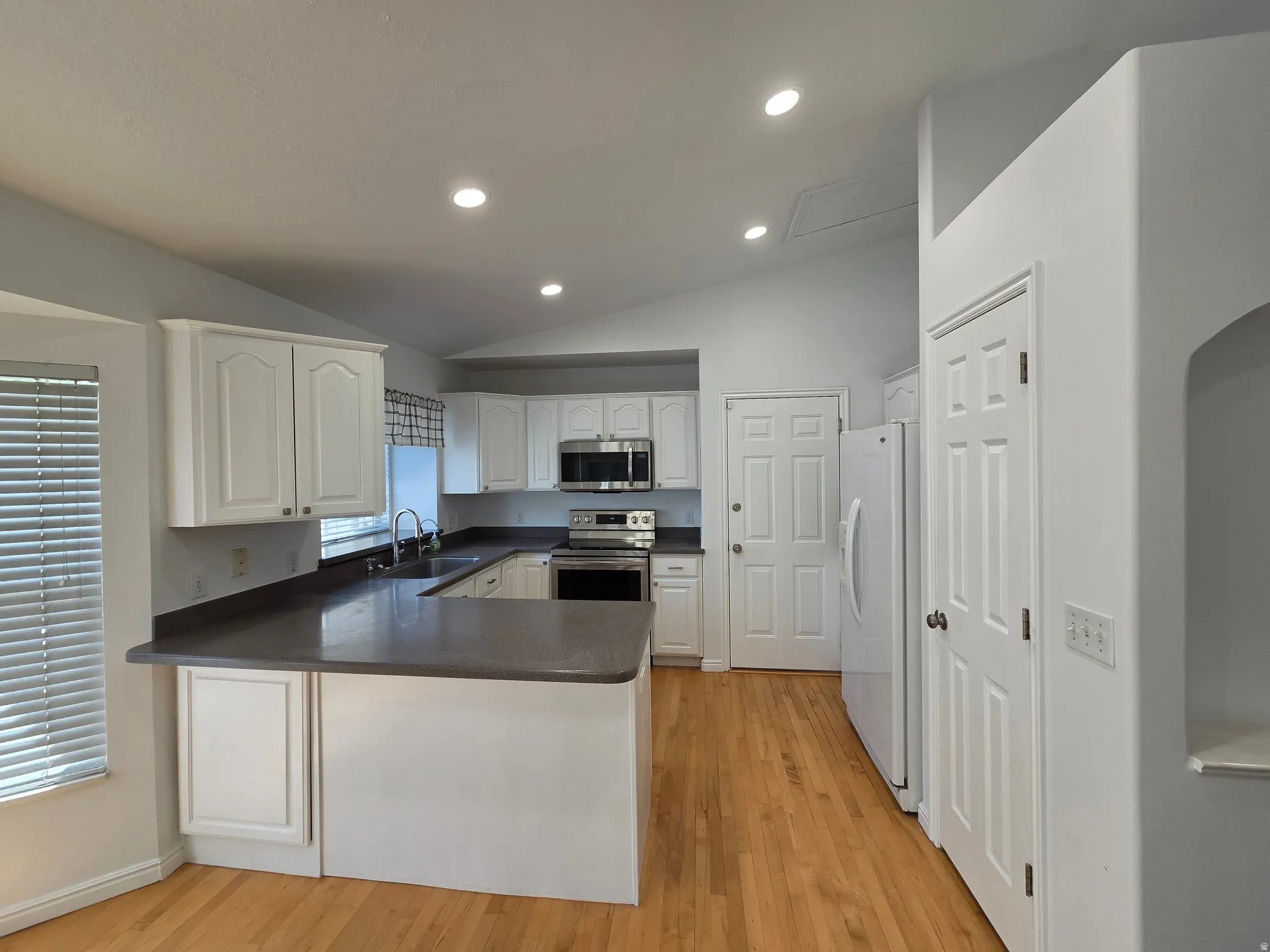 Kitchen featuring white cabinetry, dark countertops, a stainless steel microwave and range, and wood-finish flooring