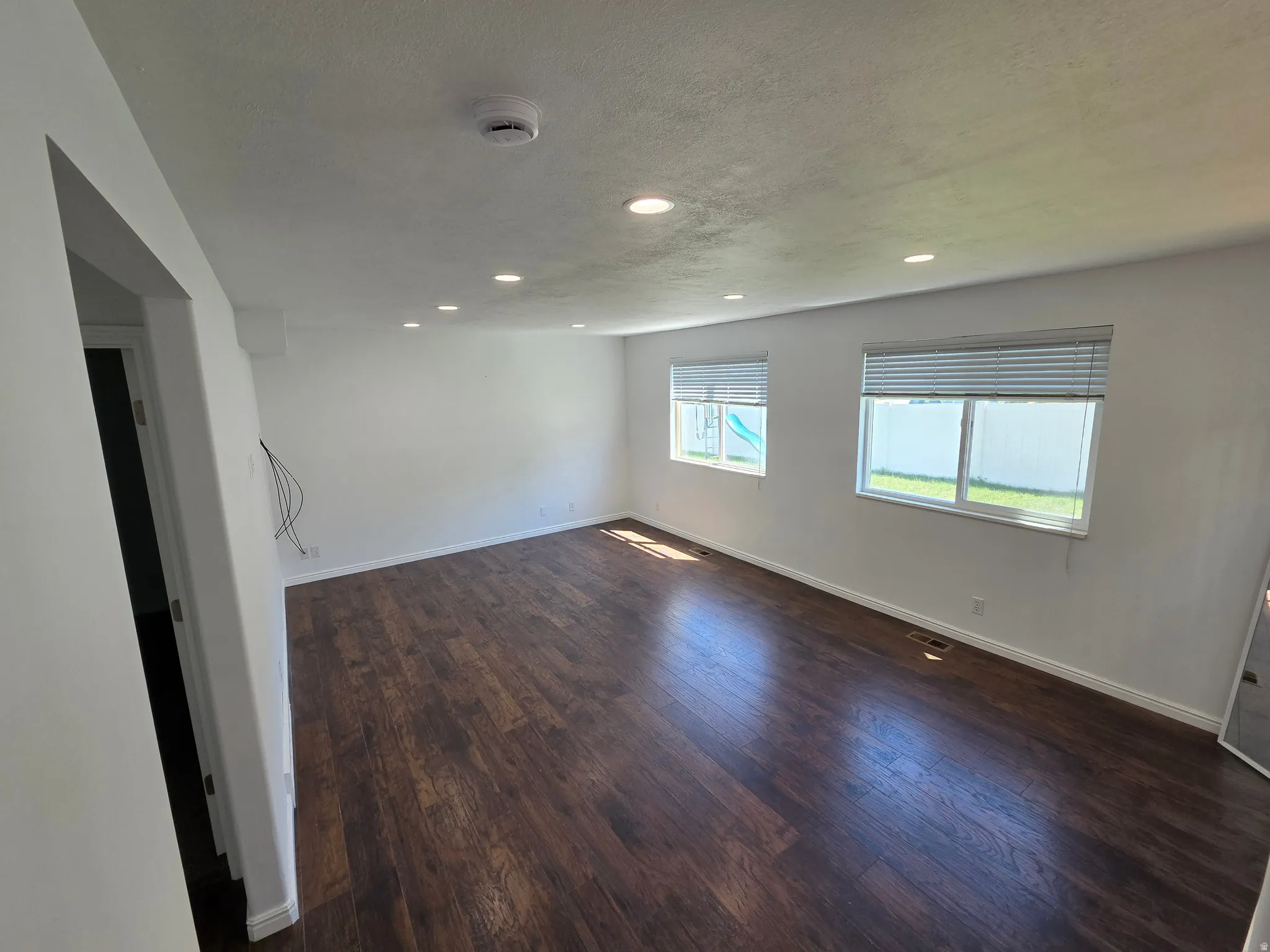 Spacious room featuring wood-finish flooring, recessed lighting, and two windows with blinds