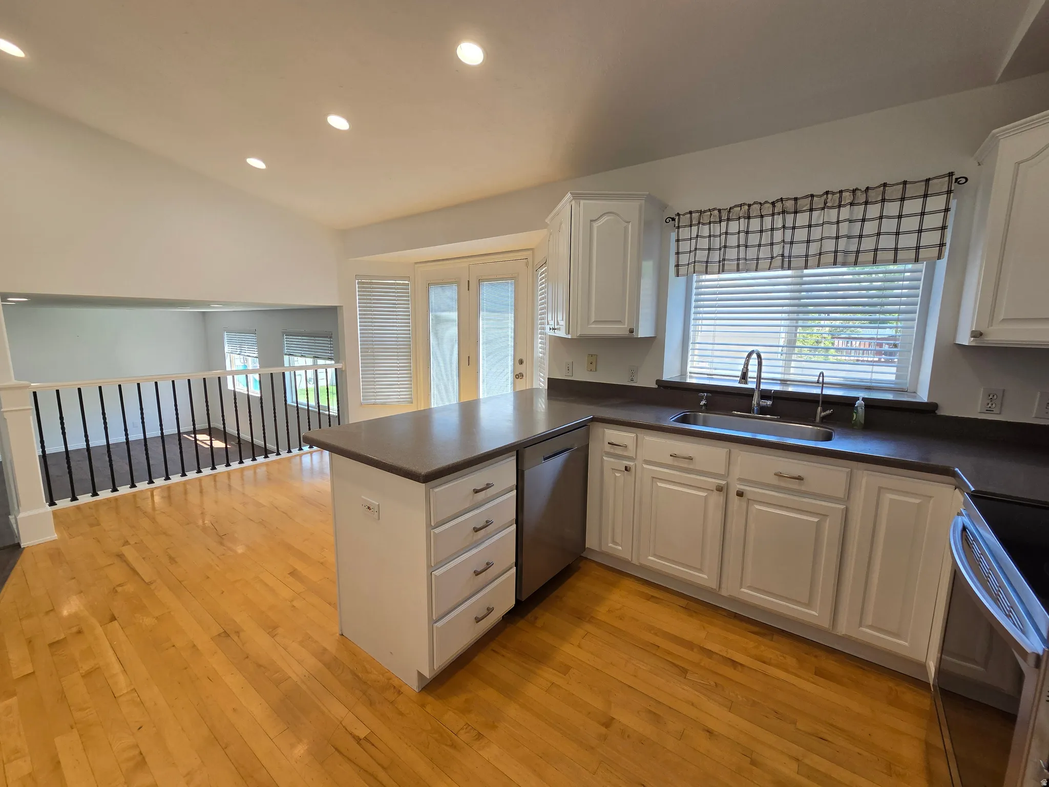 Kitchen featuring wood-finish flooring, white cabinetry, a central island with drawers, a stainless steel sink with a gooseneck faucet, and a window with horizontal blinds
