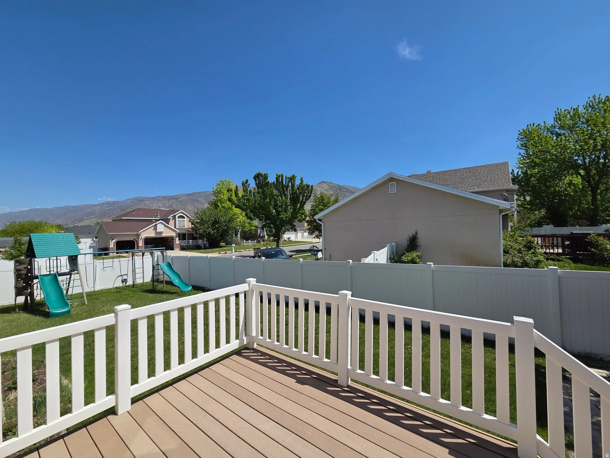 Composite decking with white railing overlooking a fenced backyard and distant mountains