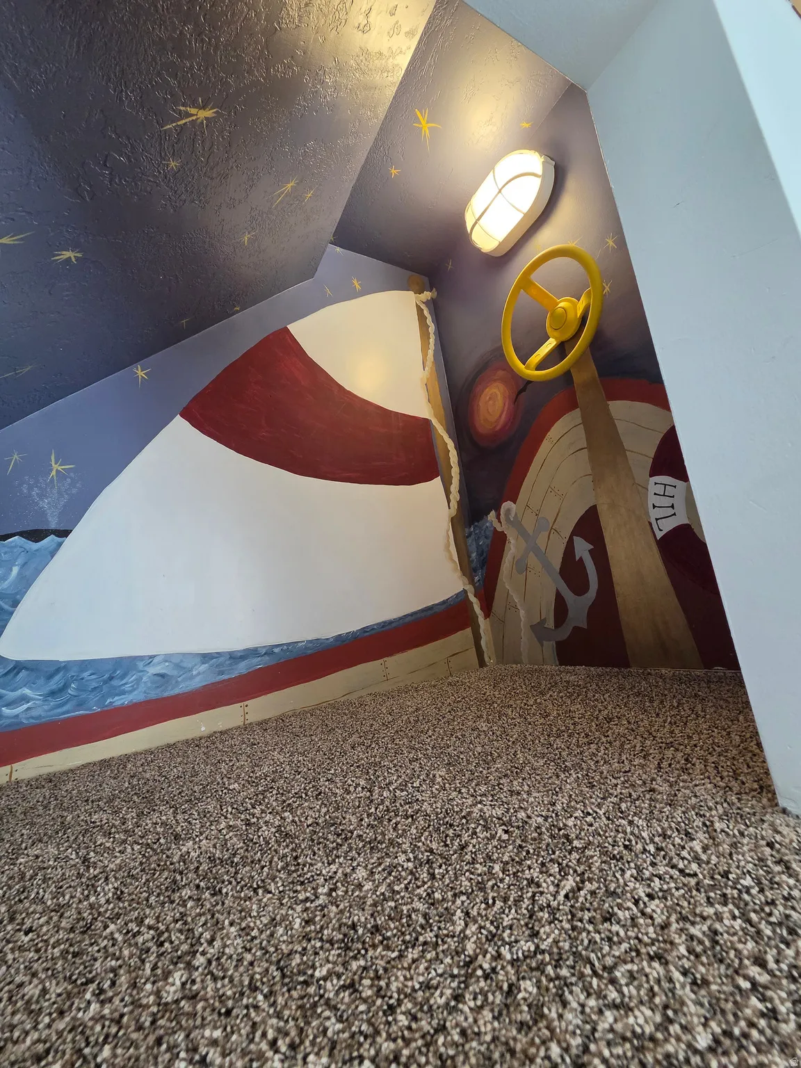 Attic space featuring custom nautical-themed wall murals, built-in wall sconce, a decorative ship's wheel, and textured carpeting