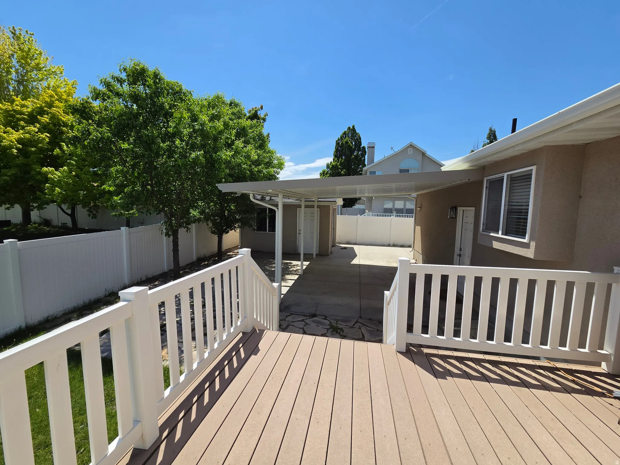Expansive wood-finish deck with white railing, featuring a covered patio area and mature perimeter trees