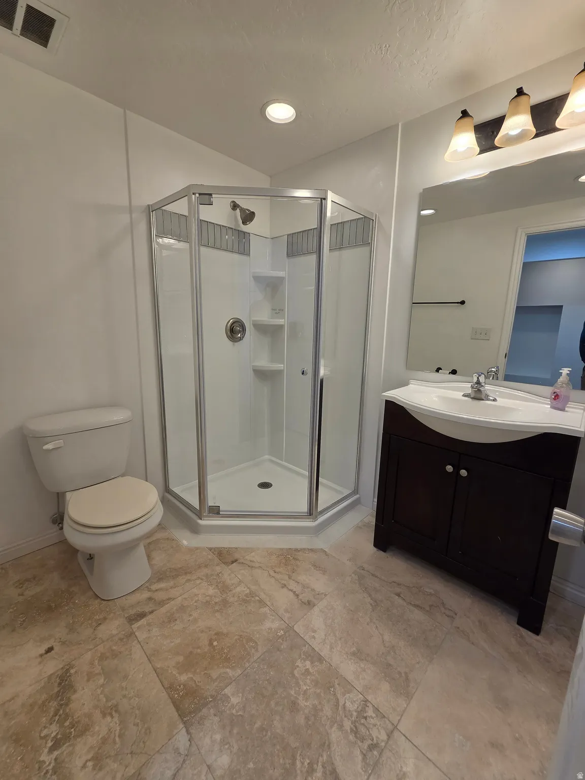 Full bathroom featuring a corner shower with glass enclosure, single vanity with a dark wood-finish cabinet, and a large wall mirror