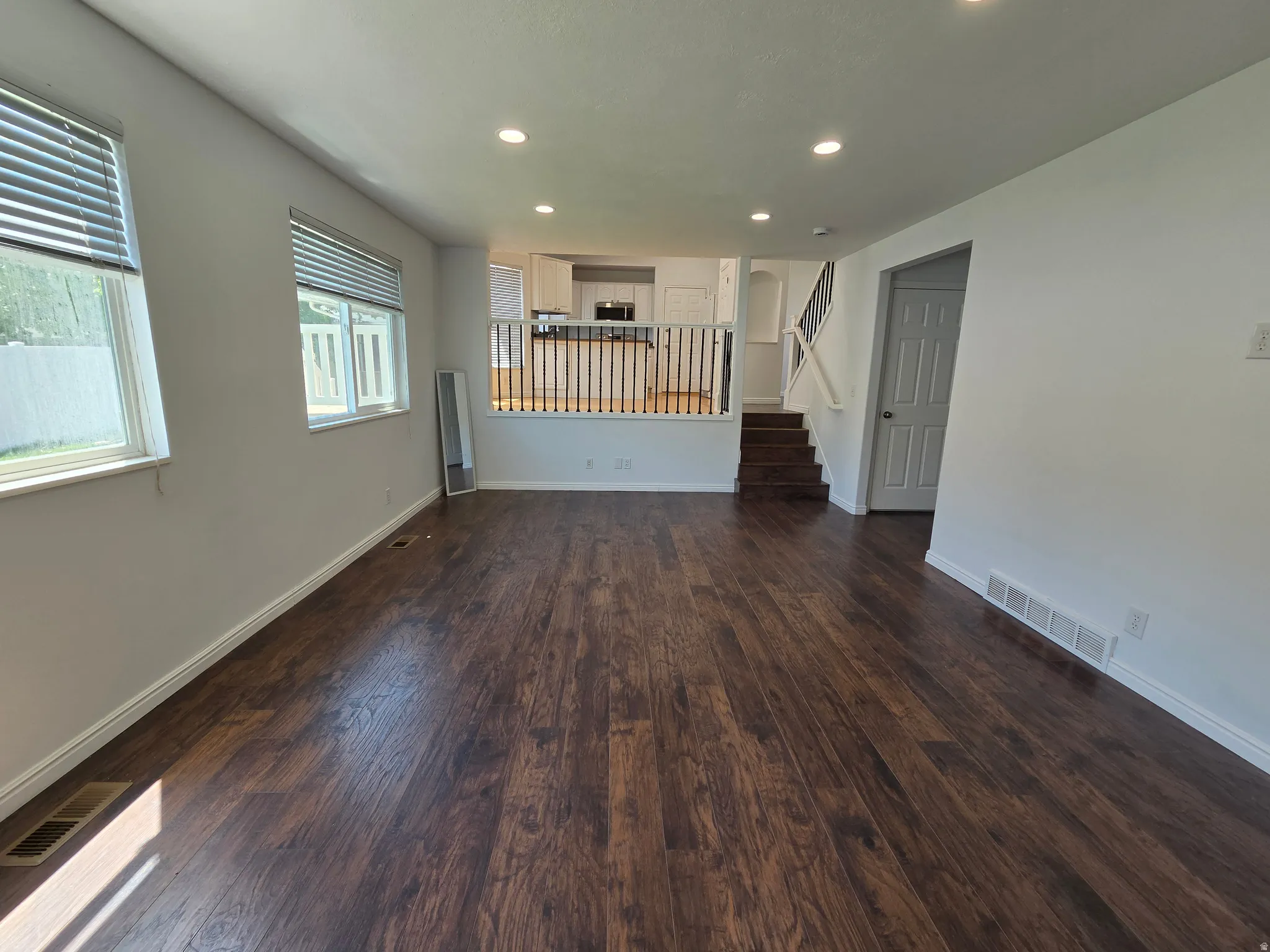 Spacious living area featuring rich wood-finish flooring, recessed lighting, and multiple windows with horizontal blinds