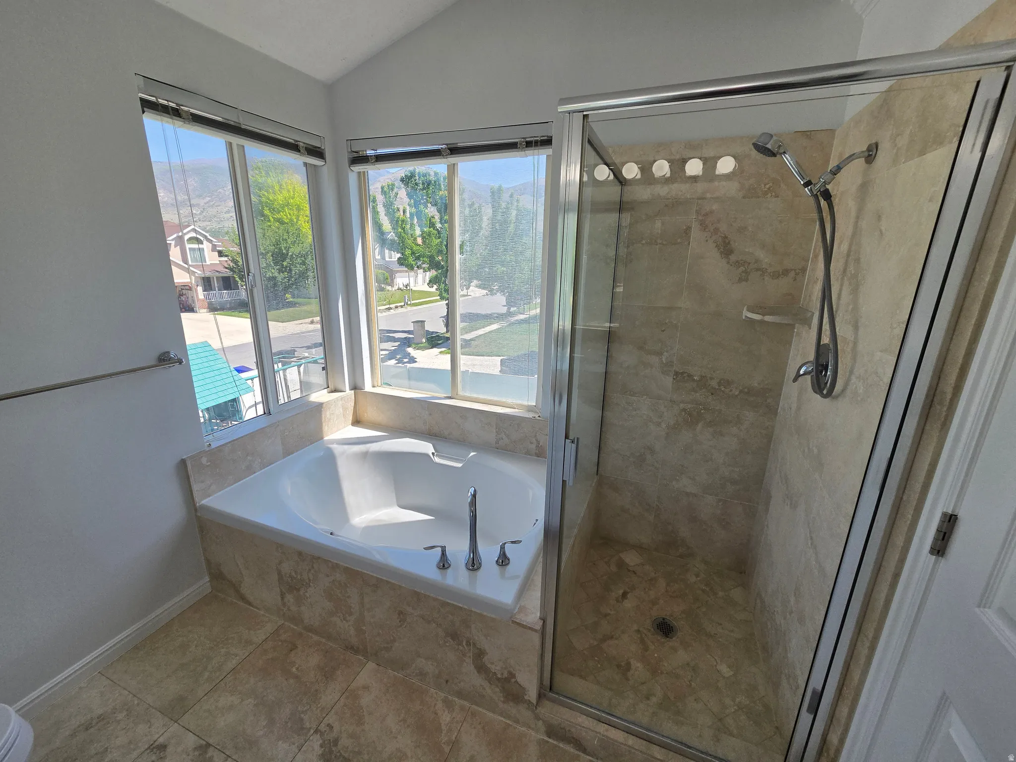 Spa-like bathroom with a built-in jetted tub, expansive windows, and a glass-enclosed shower featuring natural stone-finish tiling and a wall-mounted shower system