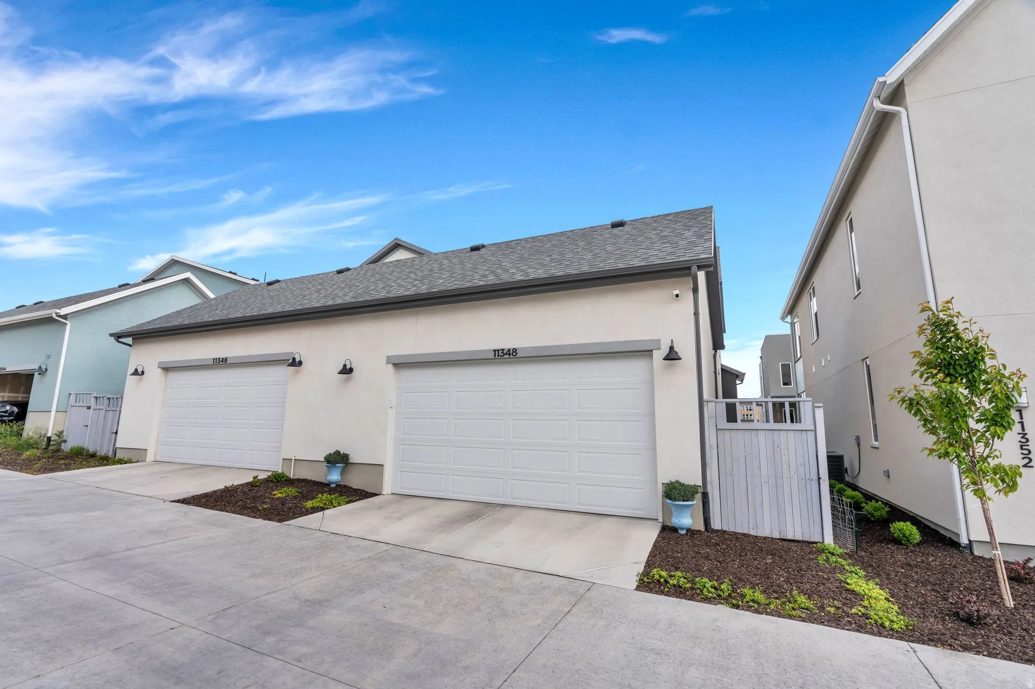 Modern stucco exterior featuring two garage doors, dark shingle roofing, and contemporary exterior lighting fixtures