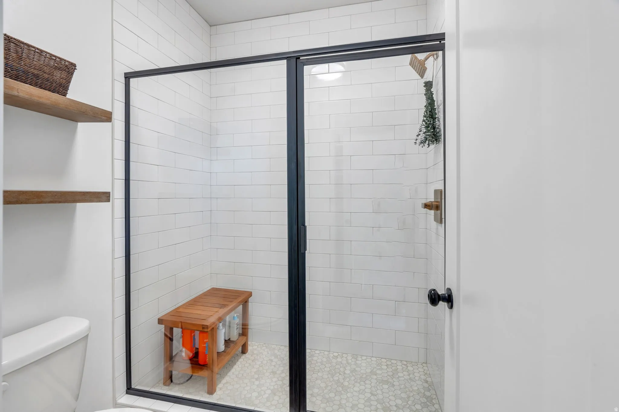 Walk-in shower with clear glass enclosure and black trim, featuring white subway tile walls and a mosaic tile floor
