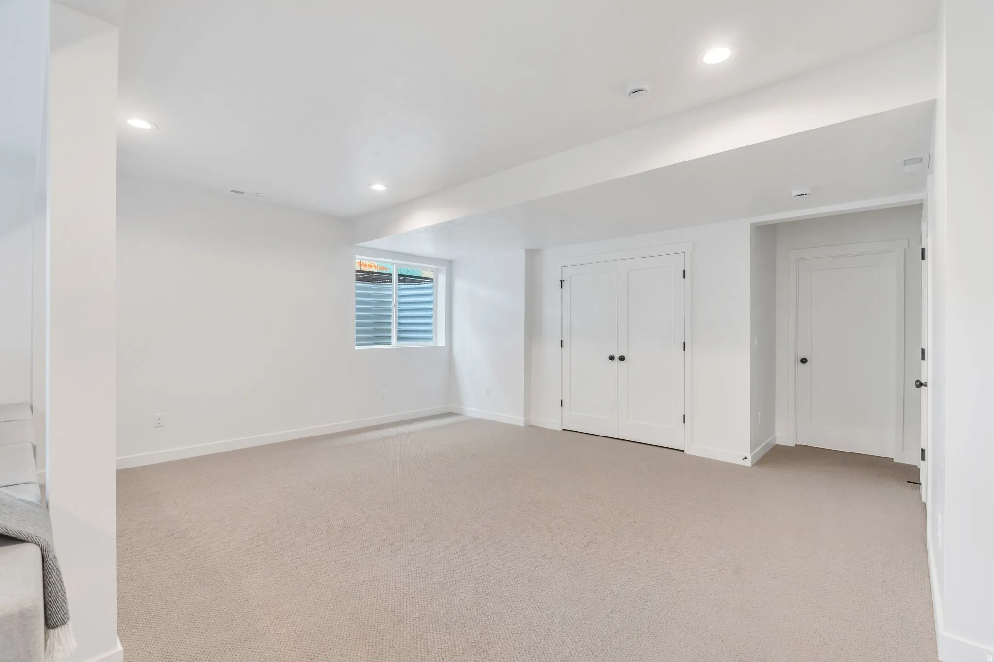 Spacious room featuring neutral carpeting, white walls, recessed lighting, and a daylight window