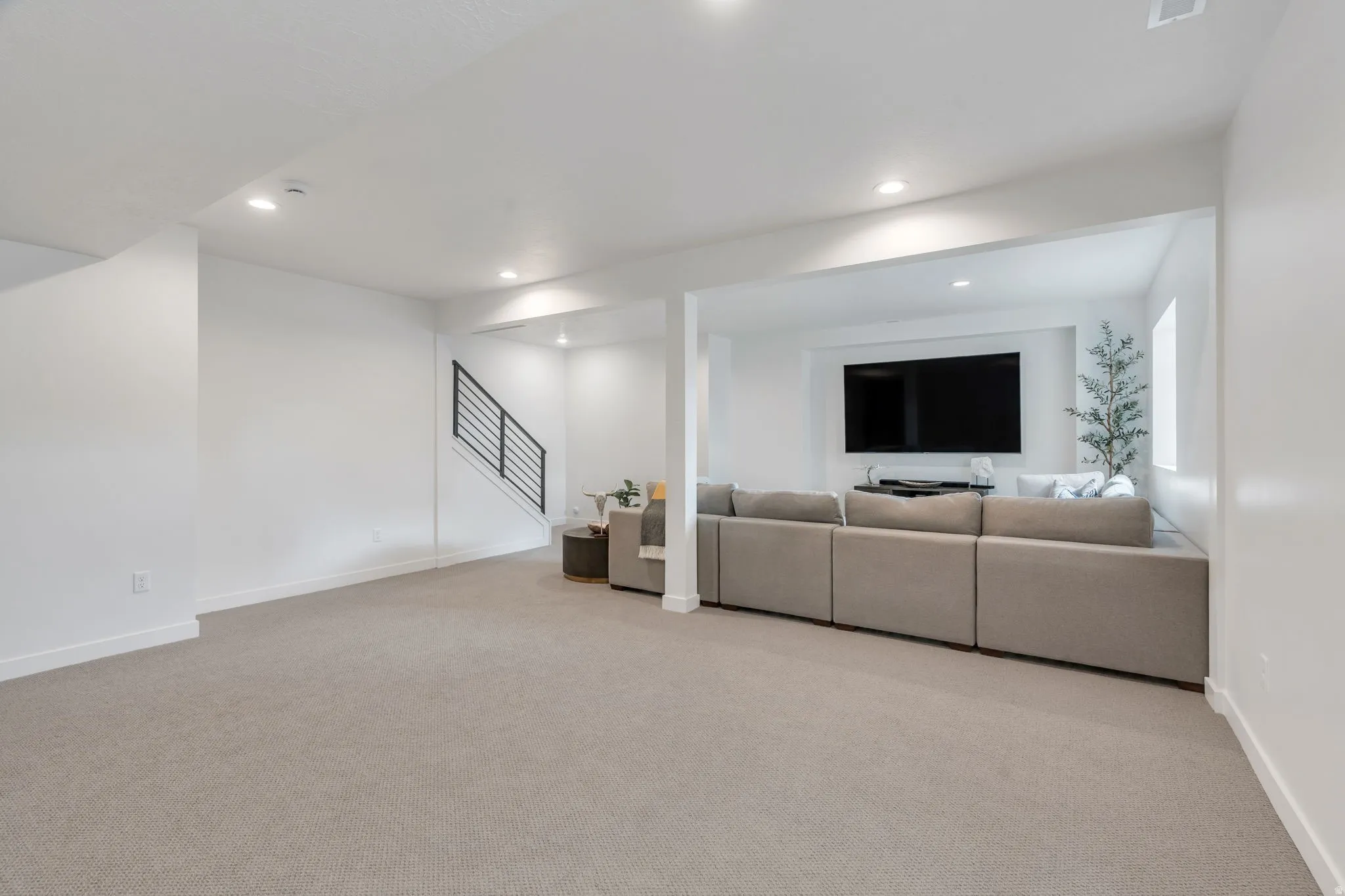 Spacious lower-level area featuring light-toned carpeting, recessed lighting, and a contemporary black metal stair railing