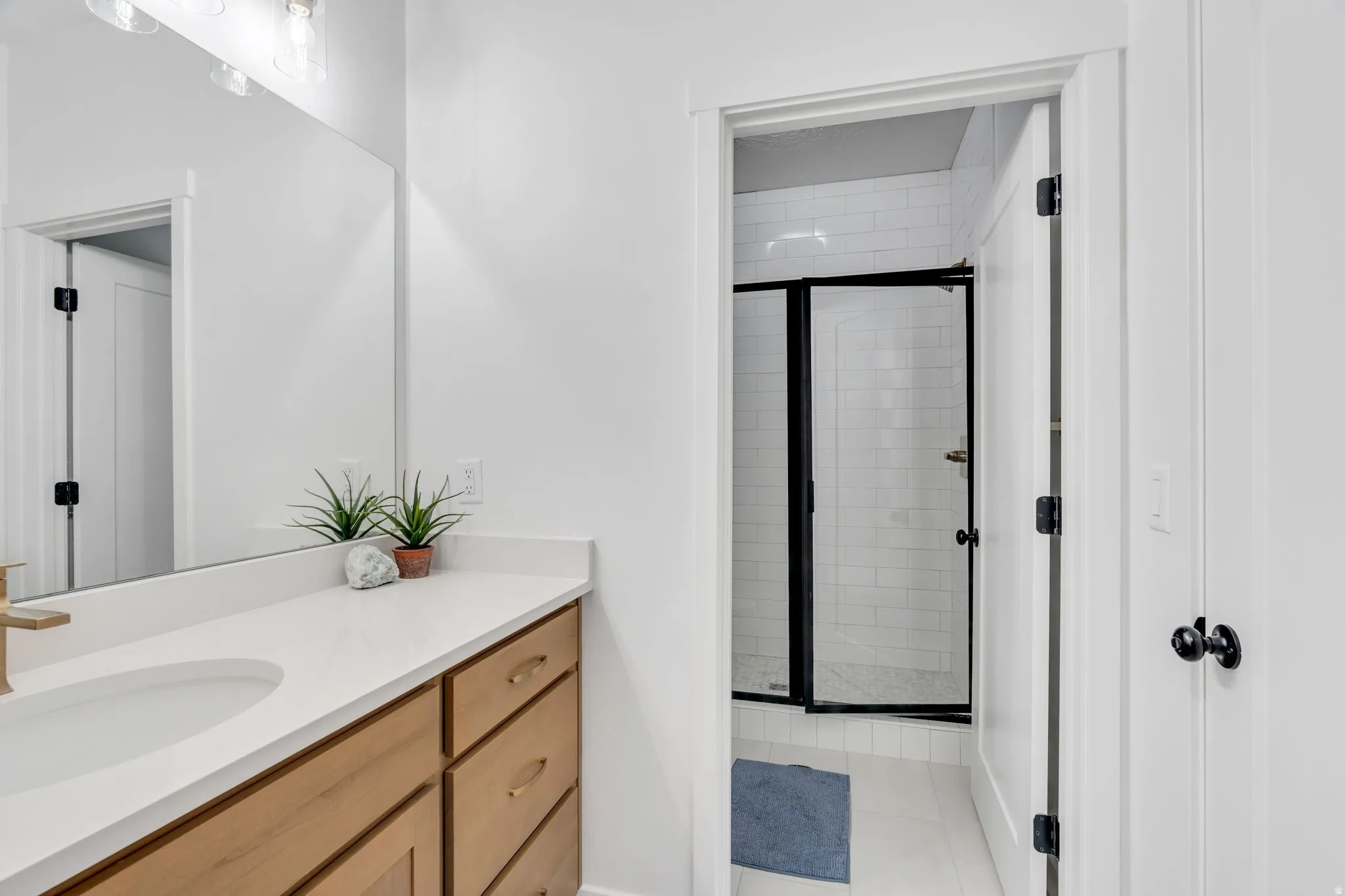 Bathroom featuring light wood-finish vanity cabinetry with brushed gold hardware, a white countertop, an undermount sink, and a large wall mirror