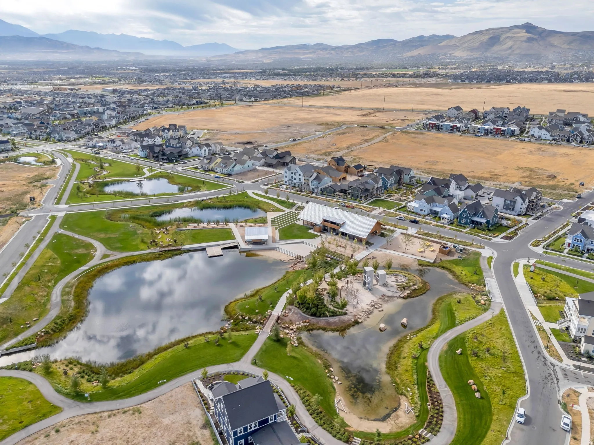 Expansive community parkland featuring multiple ponds, manicured green spaces, paved walking paths, and a community building with a covered outdoor area