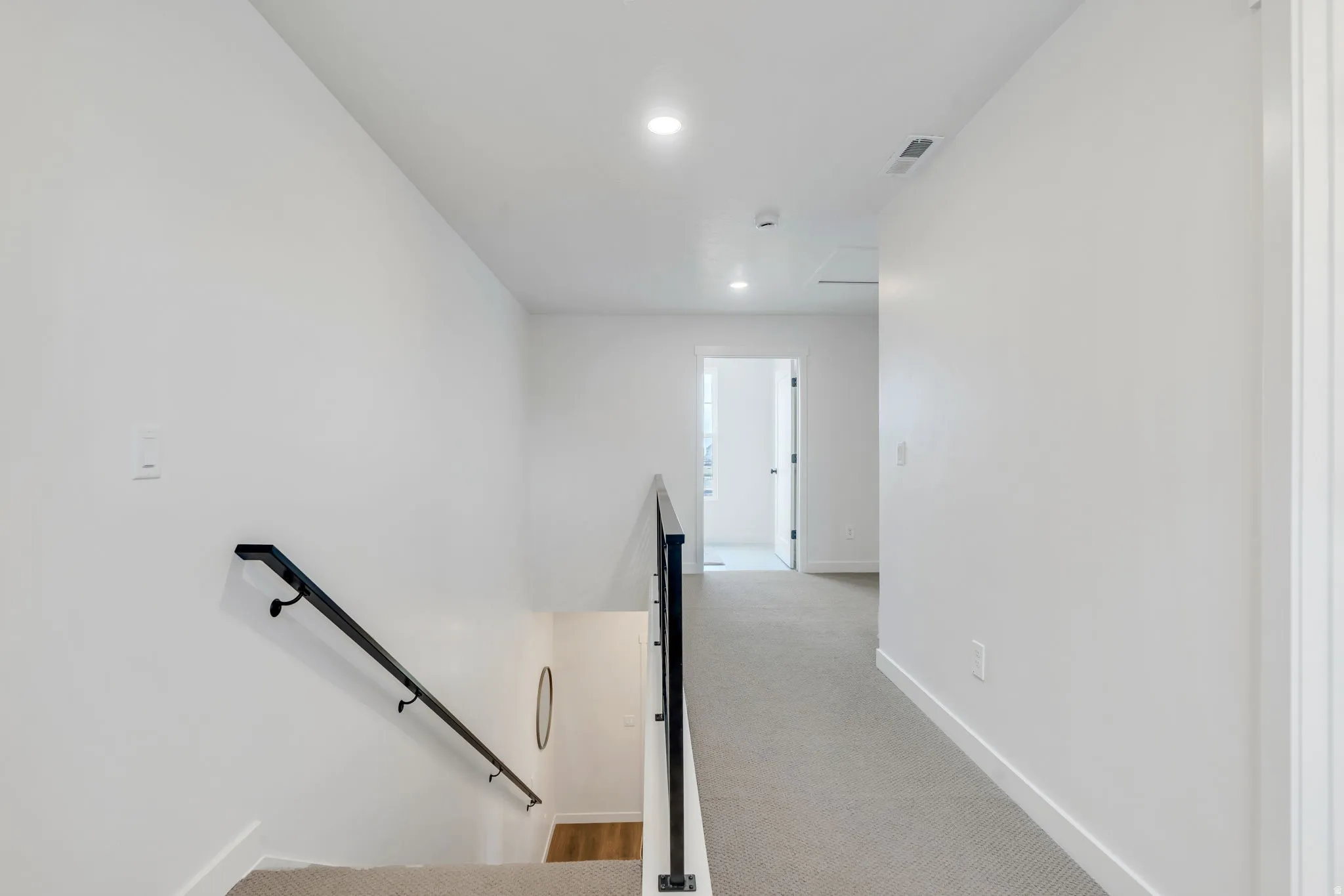 Stairwell with black metal handrails, white walls, recessed lighting, and grey carpeted flooring