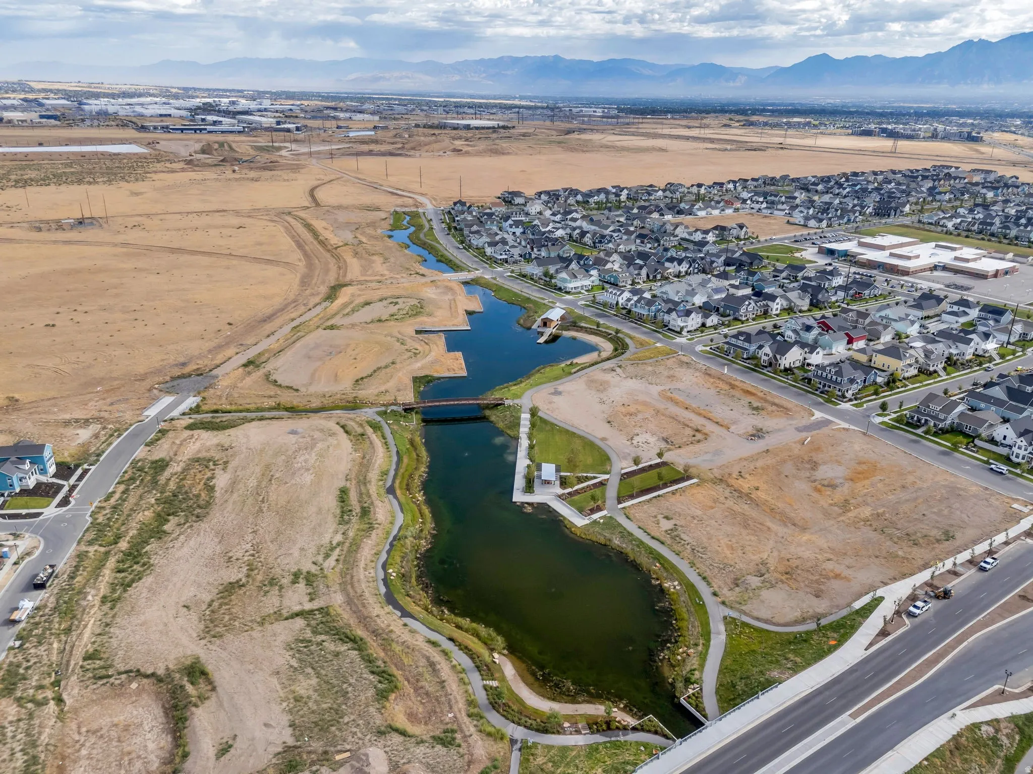 Aerial perspective of a developing residential community featuring a prominent waterway, adjacent building lots, and existing modern residences