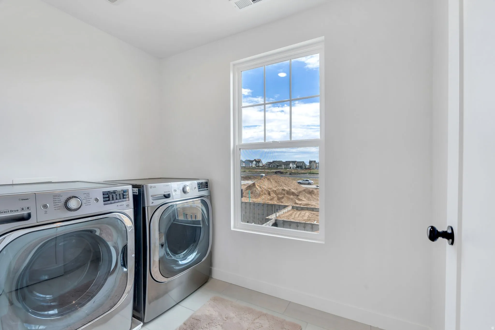 Bright laundry room featuring white walls, a white window frame, and tile flooring