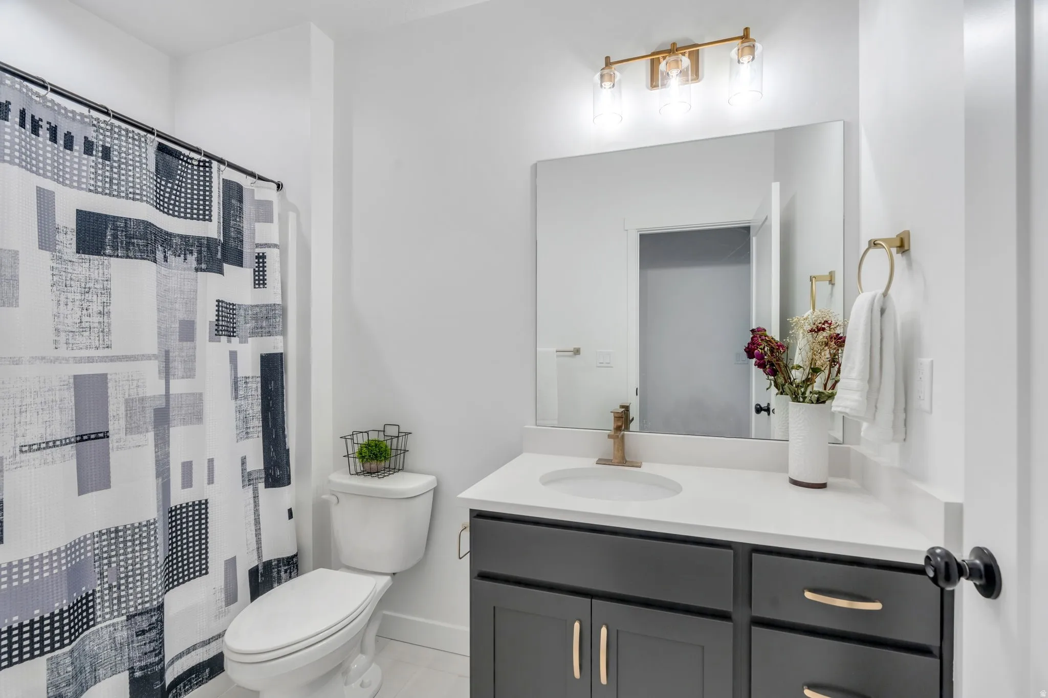 Bathroom featuring a dark gray vanity with gold hardware, a white countertop, a rectangular mirror, and a gold-finish light fixture