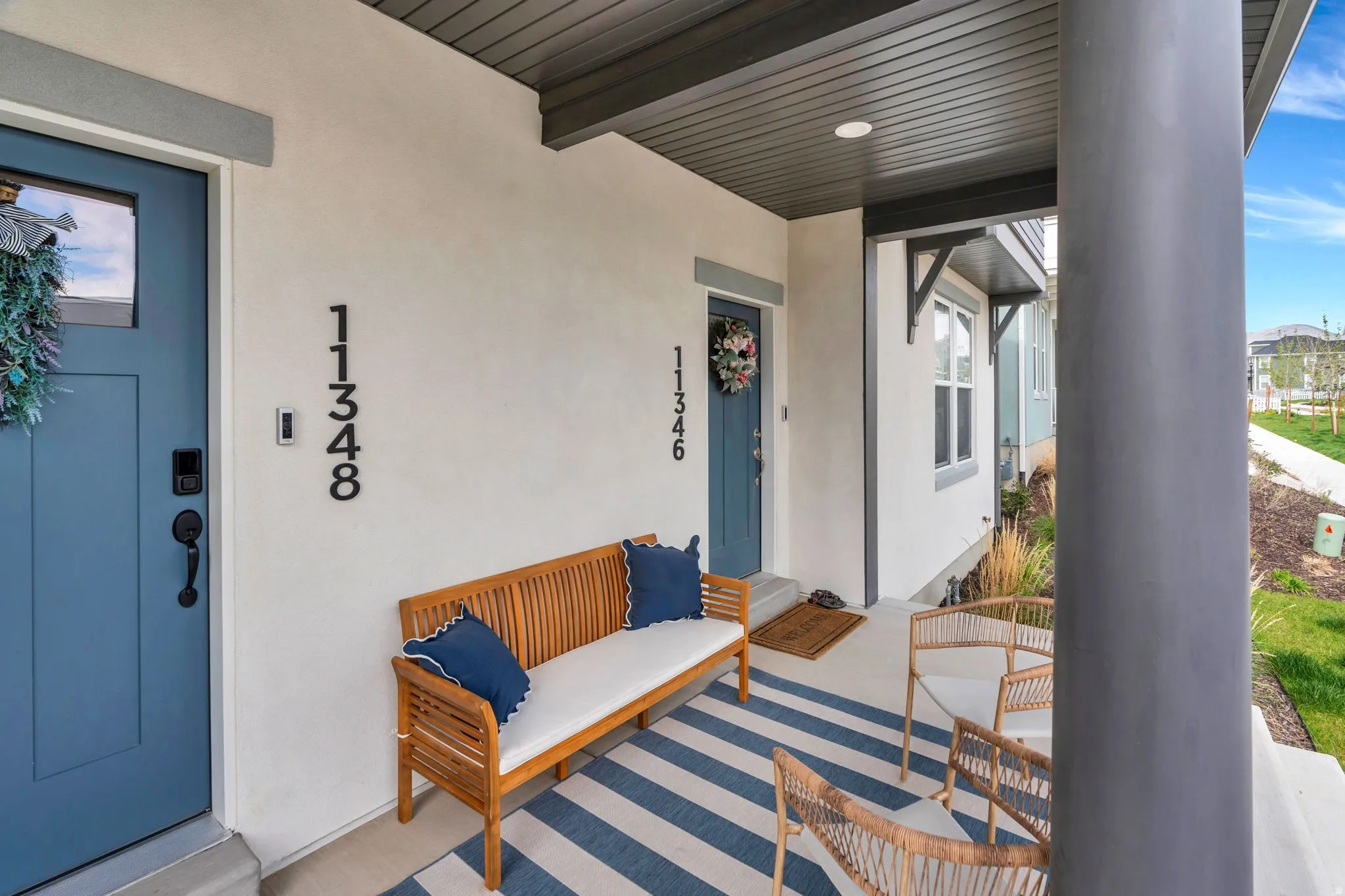 Covered front porch featuring a blue entry door with a smart lock, white stucco exterior, and dark trim accents