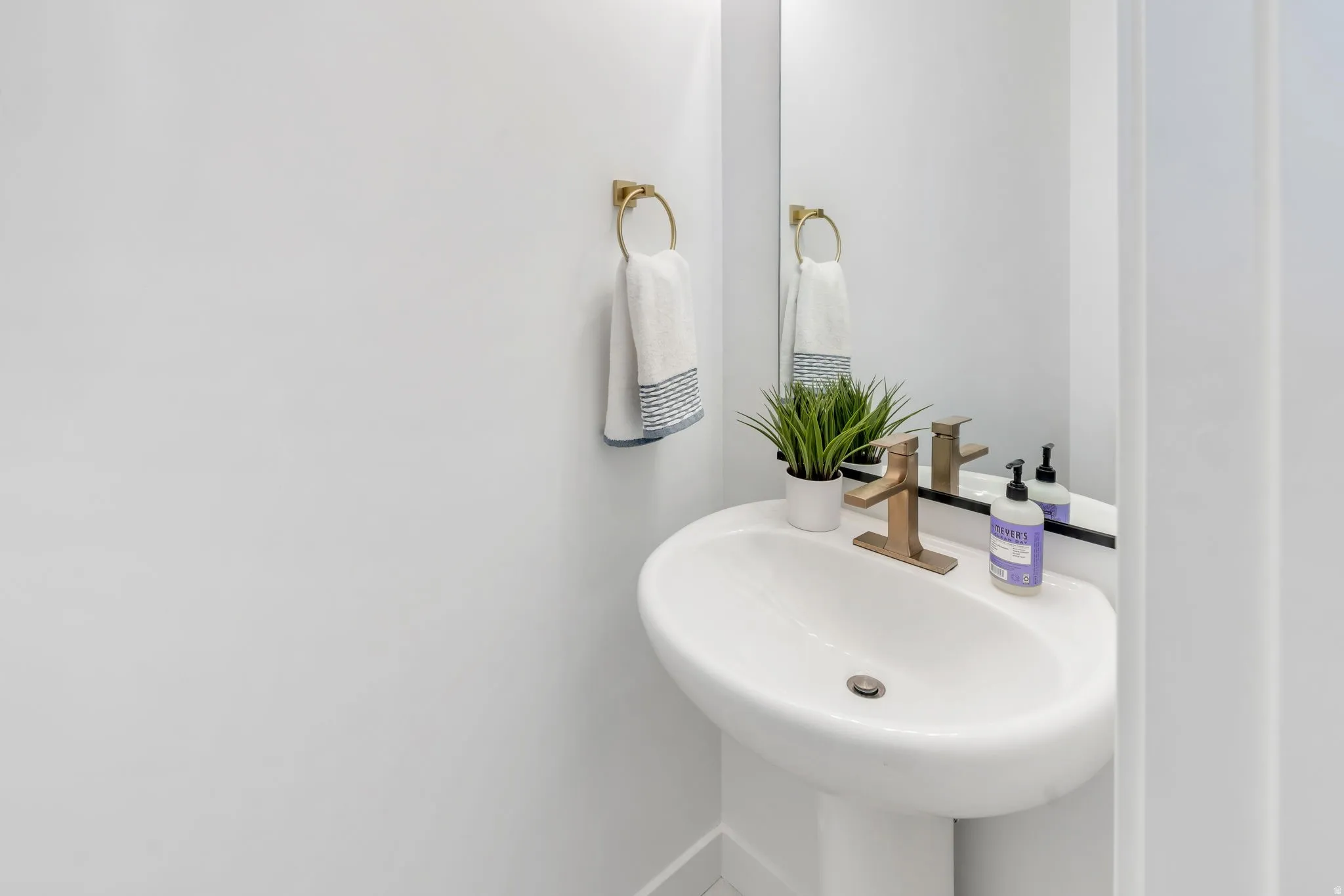 Pedestal sink with a contemporary gold-finish faucet, mirror, and towel ring