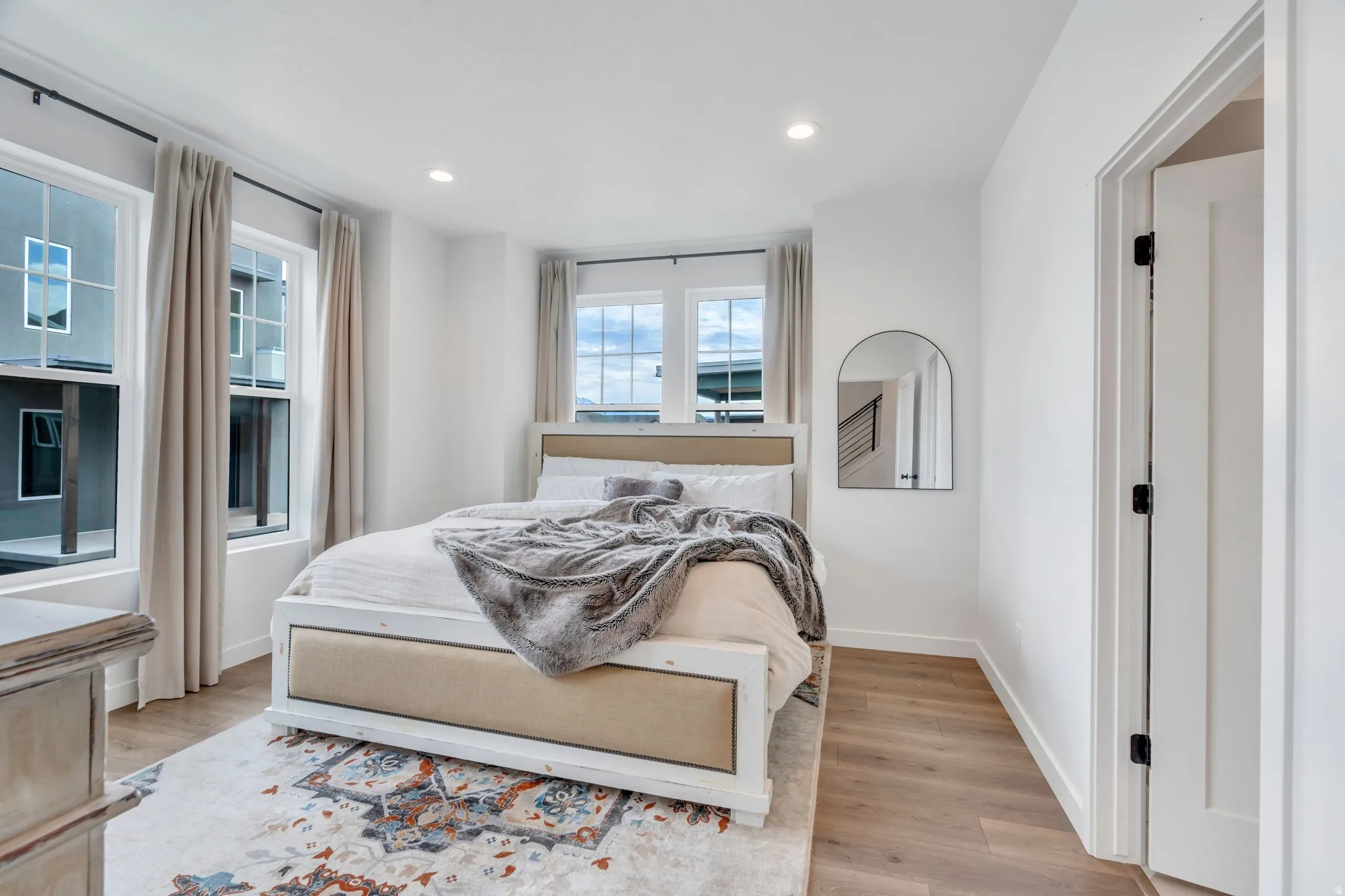 Spacious room with multiple large windows, recessed lighting, white walls, and wood-finish flooring