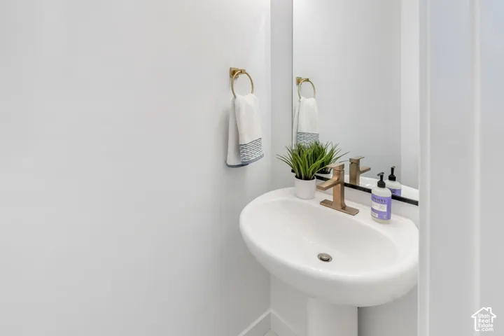 White pedestal sink featuring a metallic finish faucet, wall-mounted metallic towel ring, and a rectangular mirror