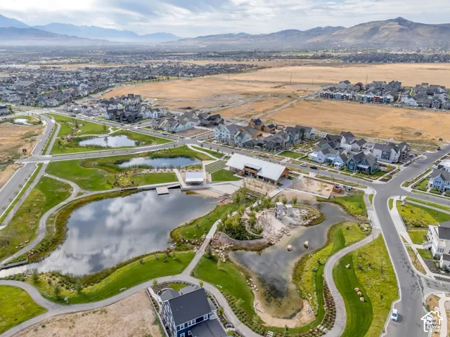 Aerial perspective of community features including multiple interconnected ponds, extensive paved walking paths, landscaped green spaces, a central clubhouse structure, and a playground